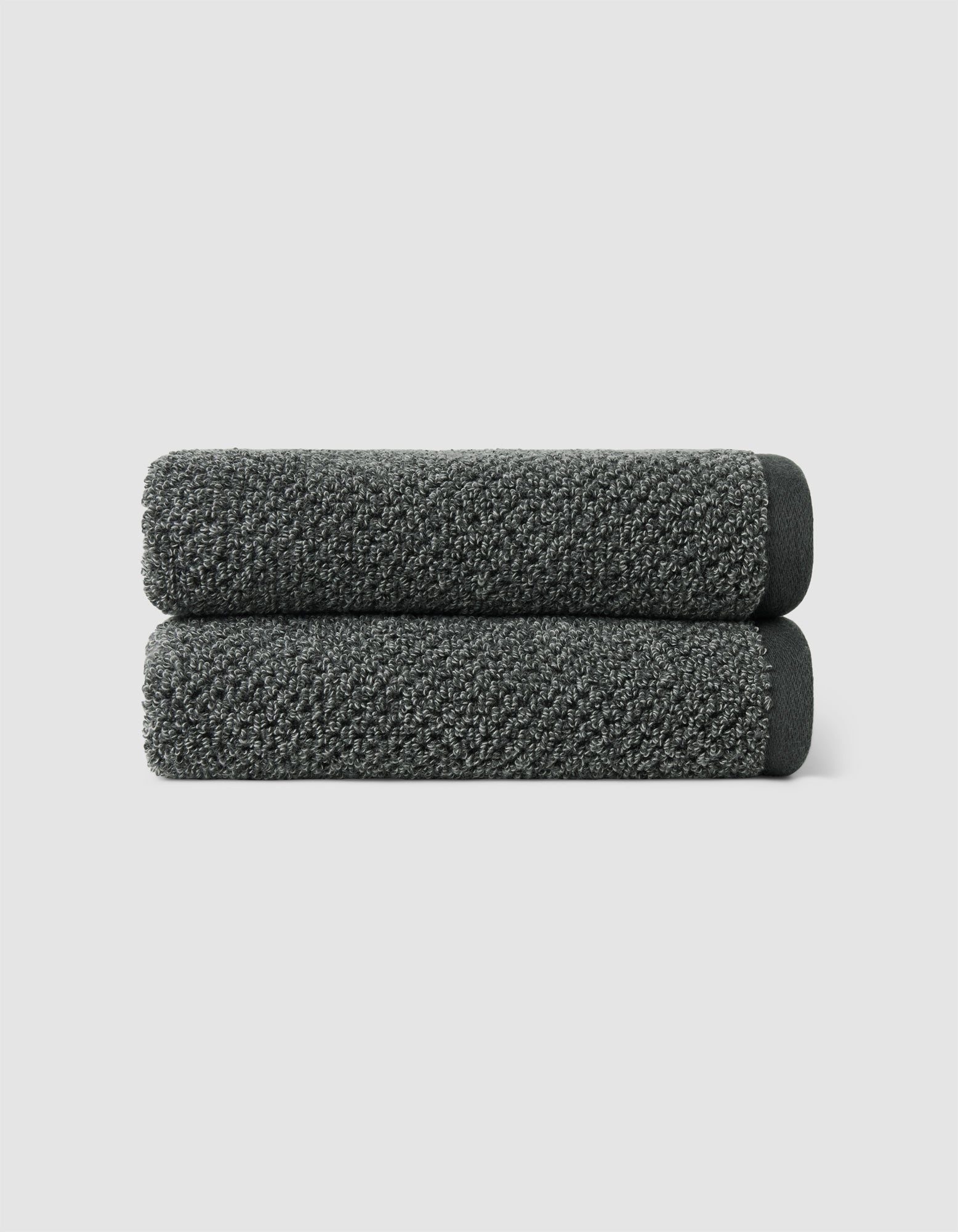Two dark gray Nantucket Hand Towels by Cozy Earth, neatly rolled and stacked, set against a plain light gray background.