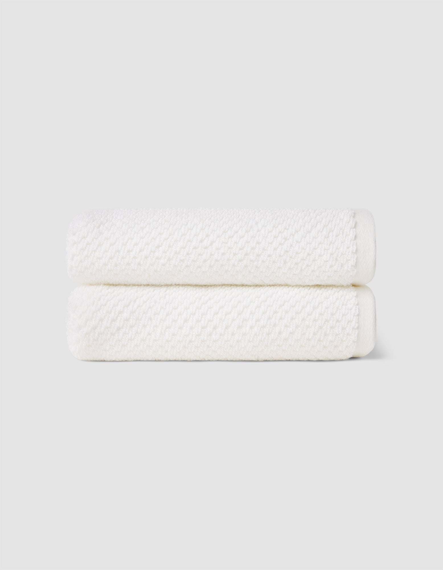 Two Nantucket Hand Towels by Cozy Earth, neatly folded and stacked, are displayed against a plain light gray background.