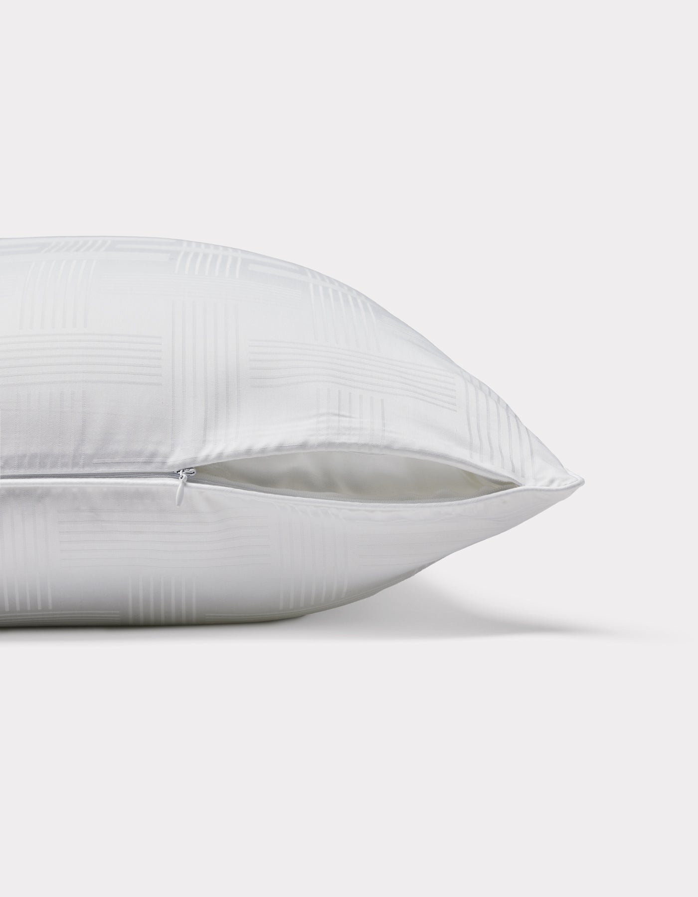 The Cozy Earth Pillow Protector is displayed lying on its side, featuring a subtle checkered pattern and a partially open zipper that reveals the inner filling. The background is plain white.