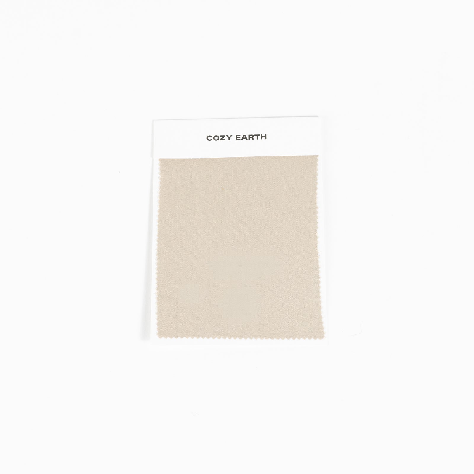 A square fabric sample from Cozy Earth, identified as the Bamboo Sheet Swatch. The swatch is a simple beige color with a zigzag edge design and is attached to a white card.