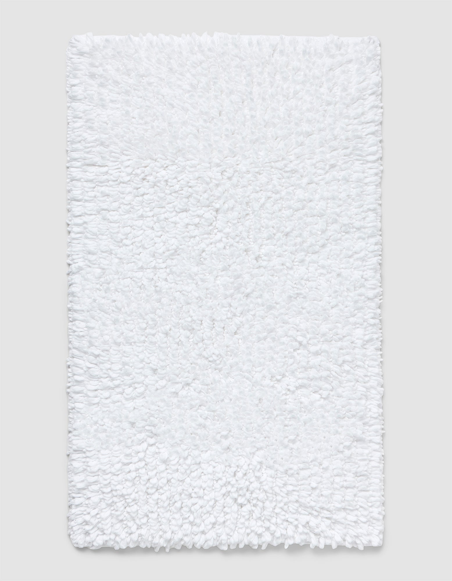 The Cozy Earth Plush Loop Bath Mat is rectangular, white, and features a soft, fluffy chenille shag texture. Shown on a plain light background, it offers plush comfort with its textured surface.