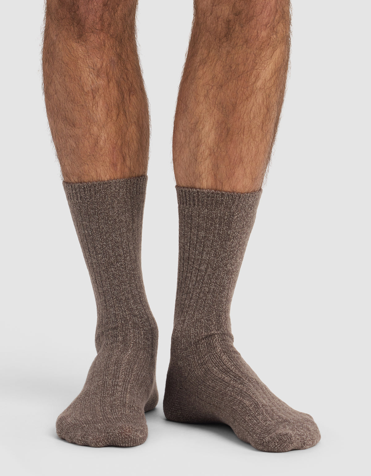 A close-up of a person's lower legs and feet wearing Cozy Earth’s The Plush Lounge Sock 3-Pack in brown, ribbed, crew-length style, set against a plain white background.