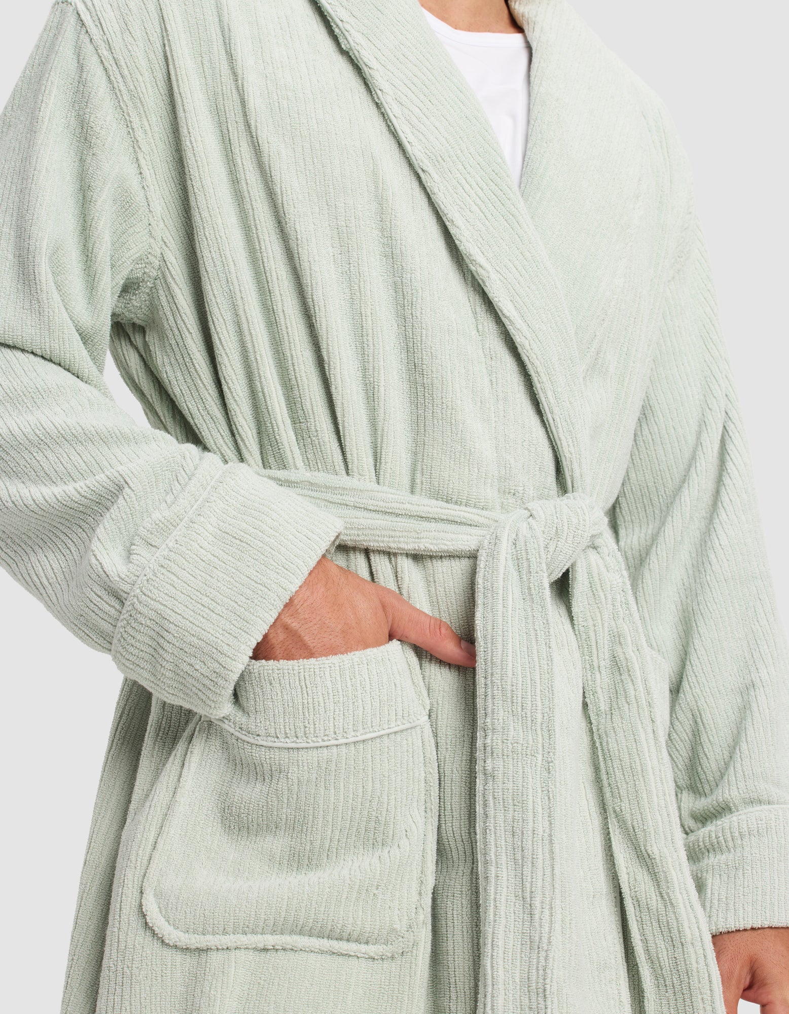 A person wearing the Cozy Earth Ribbed Terry Bath Robe in light green, belted at the waist, with one hand in the pocket and the other relaxed, stands against a plain background.