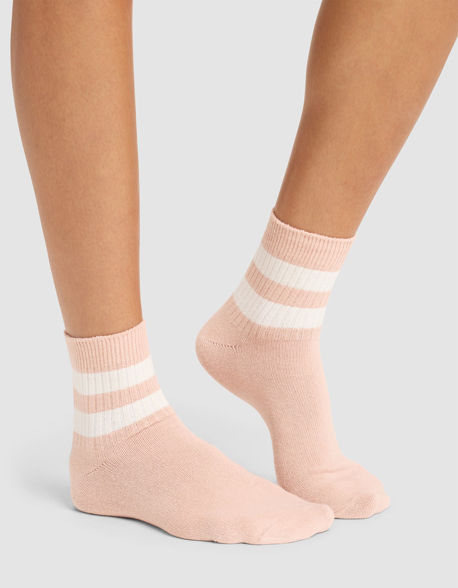 A pair of feet wears Cozy Earth Women's Sadie Socks in light pink with two white stripes near the top, standing on a light gray surface. |Color:Dusty Rose/Bone