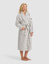 A person stands barefoot in the Cozy Earth Striped Luxe Bath Robe, white with black vertical stripes and a tie waist, hands partially in pockets, against a plain light gray background.|Color:Black Stripe