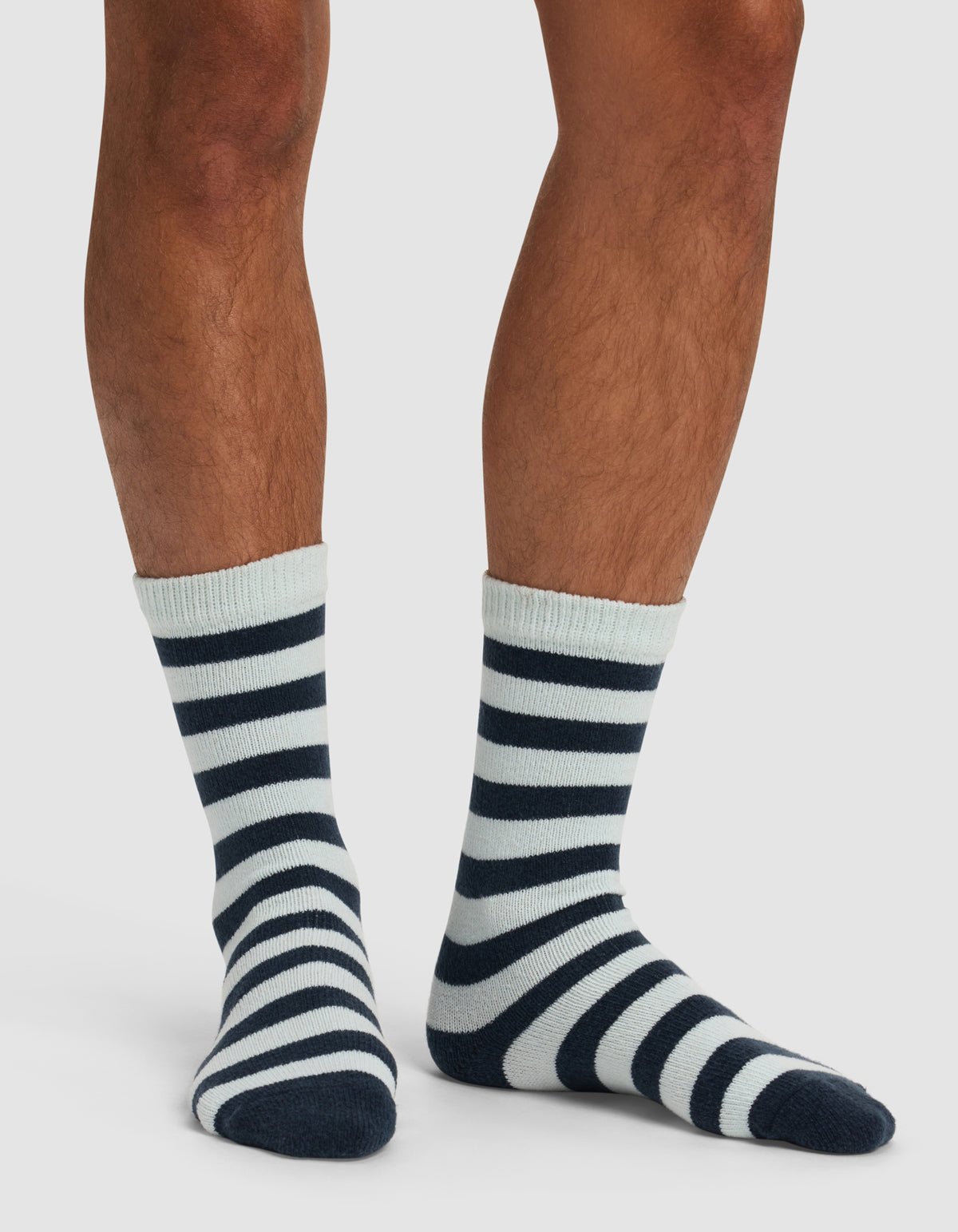 A person showcases only their lower legs and feet in Cozy Earth's The Striped Plush Lounge Sock, featuring black and white stripes, against a plain white background.