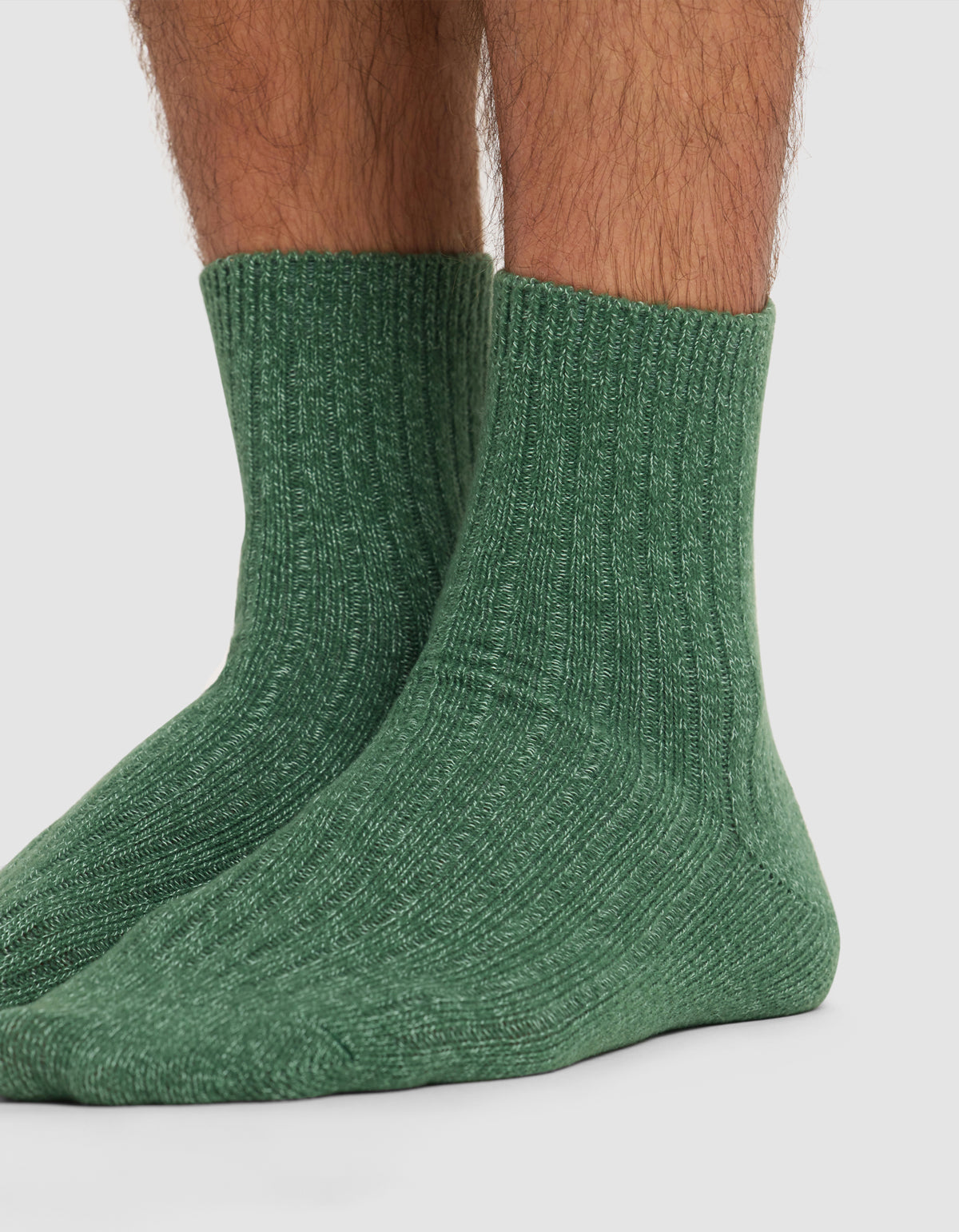 A close-up of lower legs and feet wearing Cozy Earth's Plush Modern Crew Sock 3-Pack in green, shown against a plain white background.