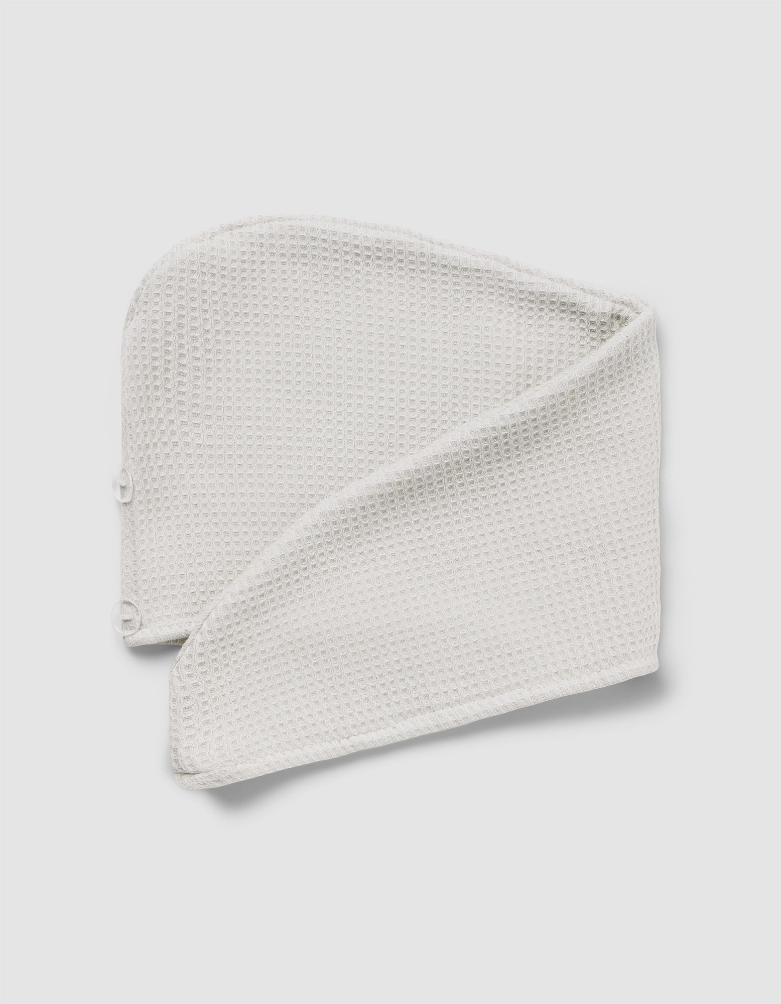 The Cozy Earth Waffle Hair Towel, a folded, textured white headband with snap buttons at one end, is displayed on a light gray background.