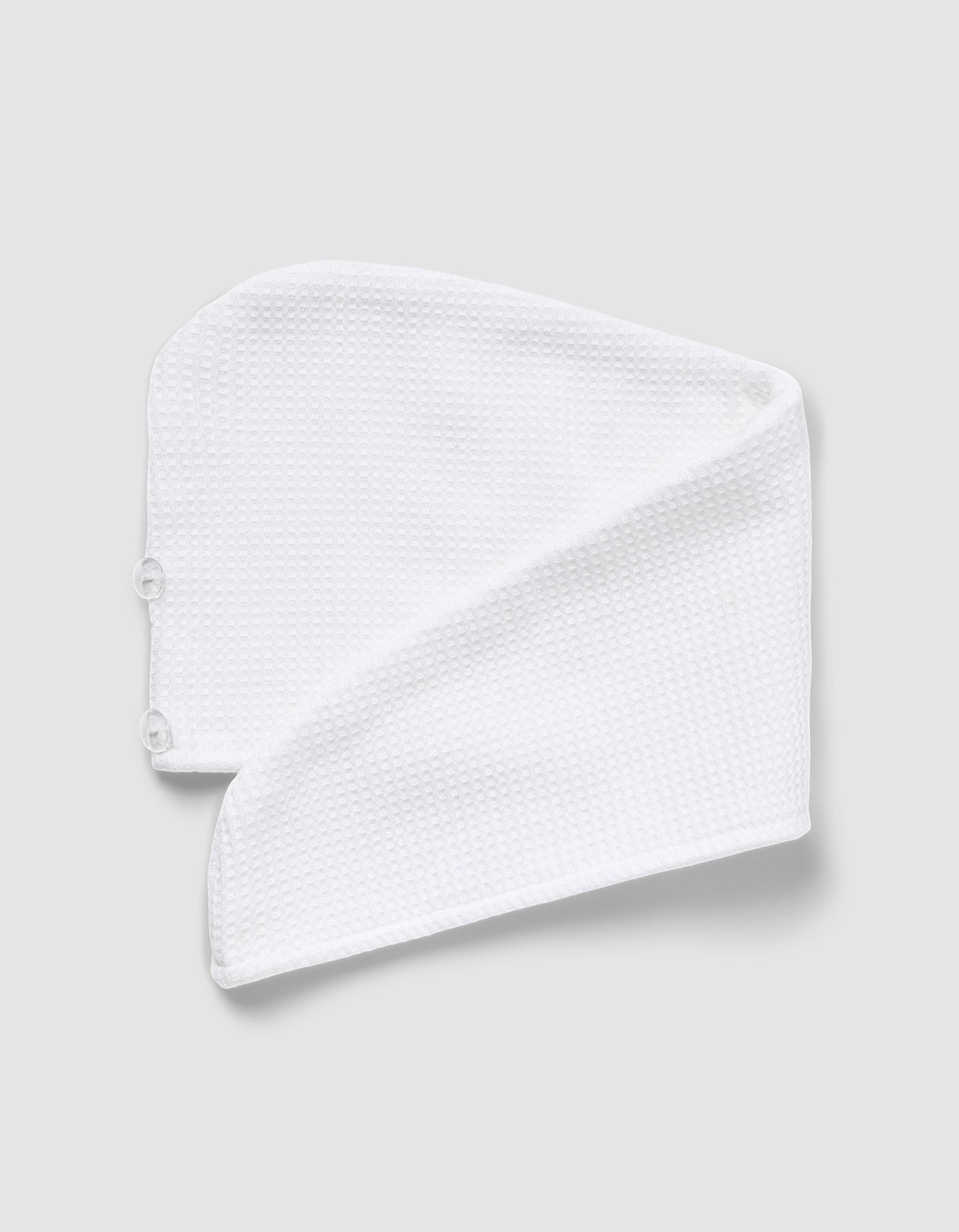 The Cozy Earth Waffle Hair Towel, made from white textured microfiber, is folded into a triangle with two buttons visible on one end and displayed against a light gray background.