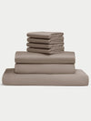 The Bamboo Bedding Core Bundle from Cozy Earth is displayed against a plain white background, featuring a neatly stacked set of folded taupe bed sheets, including pillowcases, a fitted sheet, and a flat sheet. |Color:Walnut