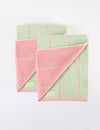 Two Windowpane Resort Towels by Cozy Earth, featuring pastel green and pink checkered patterns and small rectangular labels in the lower left corners, are stacked on a white surface. |Color:Watermelon