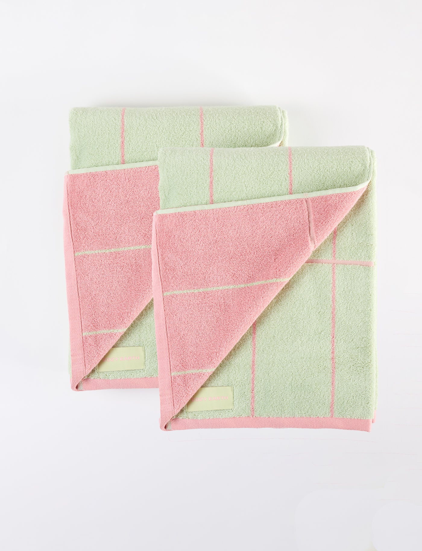 Two Windowpane Resort Towels by Cozy Earth, featuring pastel green and pink checkered patterns and small rectangular labels in the lower left corners, are stacked on a white surface. |Color:Watermelon