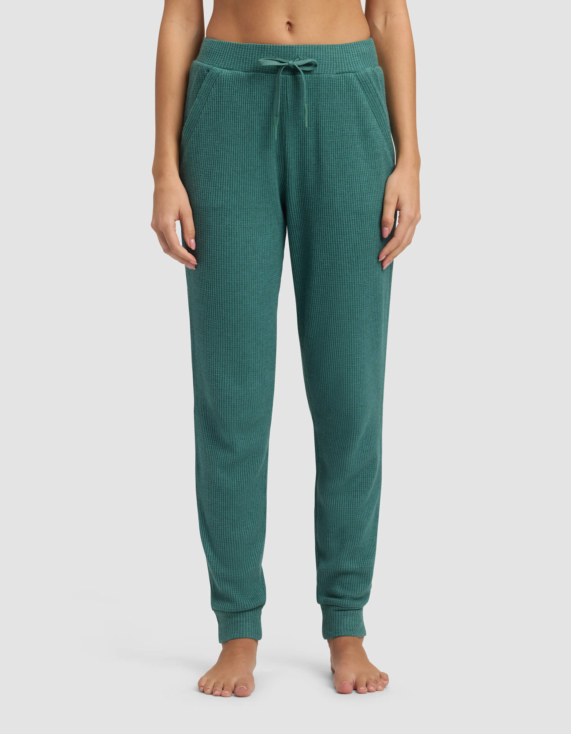 A person stands barefoot in Cozy Earth's Women's Blake Waffle Jogger, featuring a ribbed texture, green color, drawstring waist, and side pockets; shown from waist to feet against a plain light background.|Color:Sea Green
