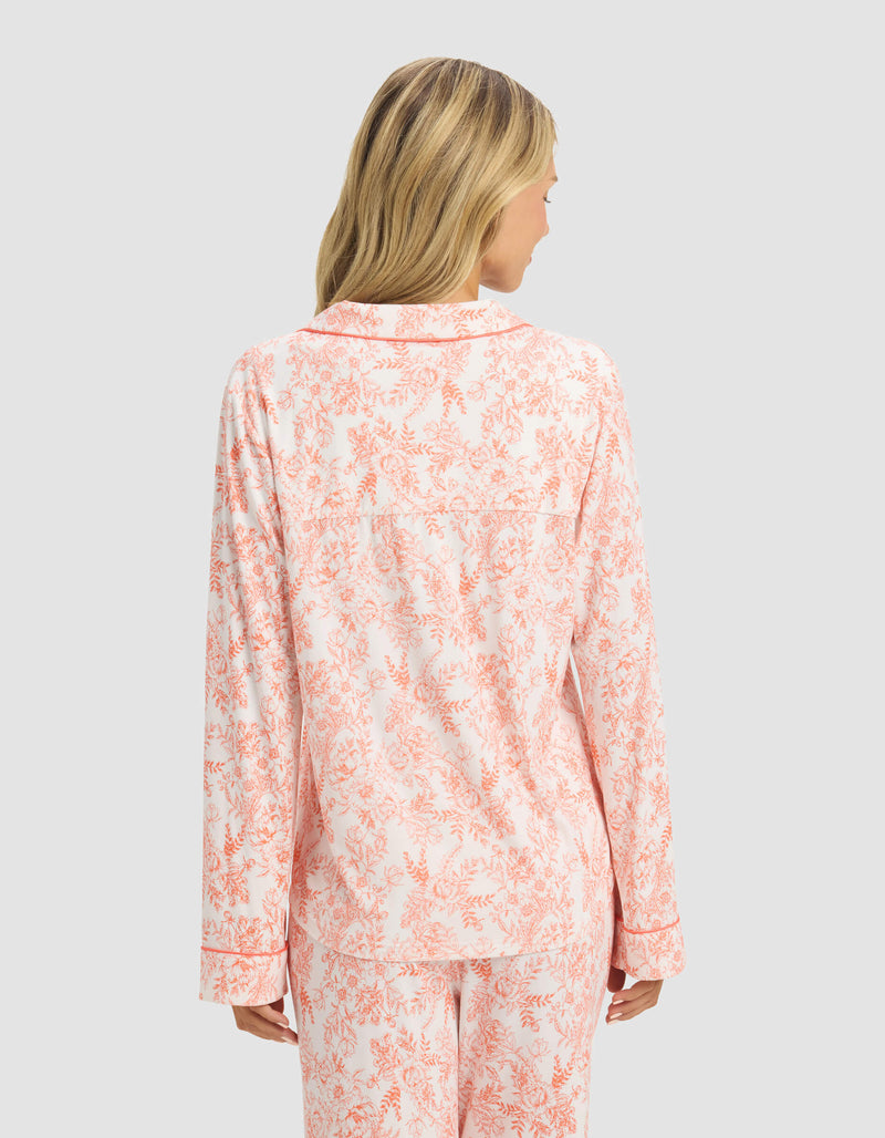 A woman with blonde hair is seen from the back wearing Cozy Earth’s Women's Bamboo Stretch-Knit Long Sleeve Pajama Top in a light pink and white floral print, paired with matching pants, against a plain light gray background.