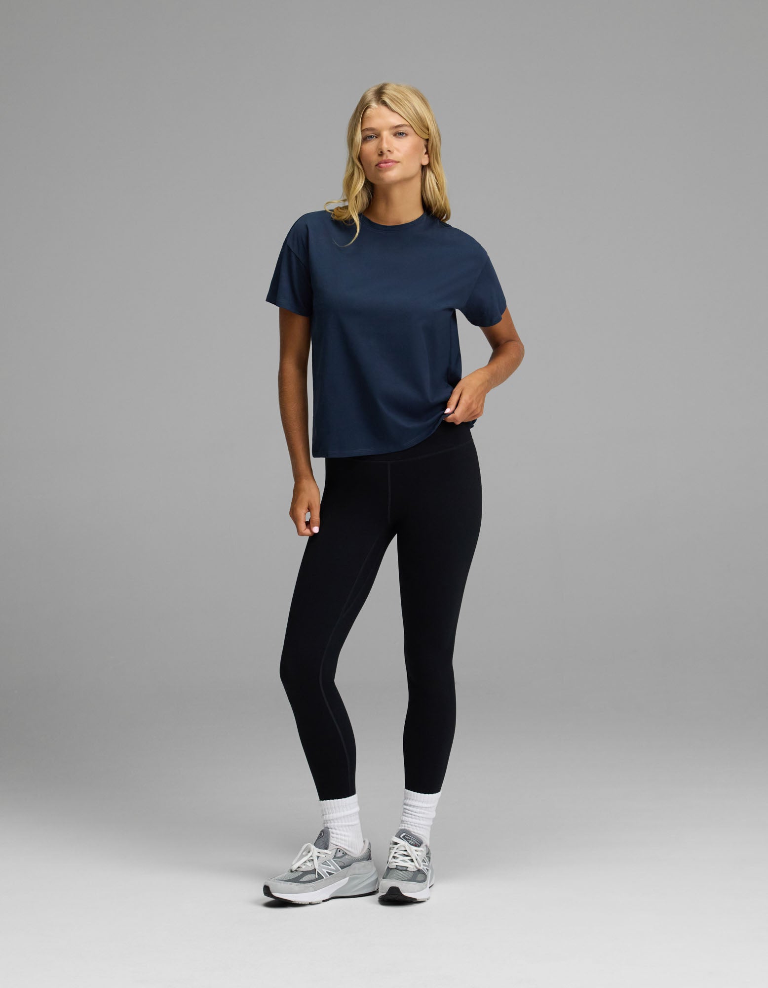 A person wearing the Cozy Earth Women’s All Day Tee in navy, black leggings, white socks, and gray sneakers stands against a plain gray background with one hand on their hip.|Color:Eclipse