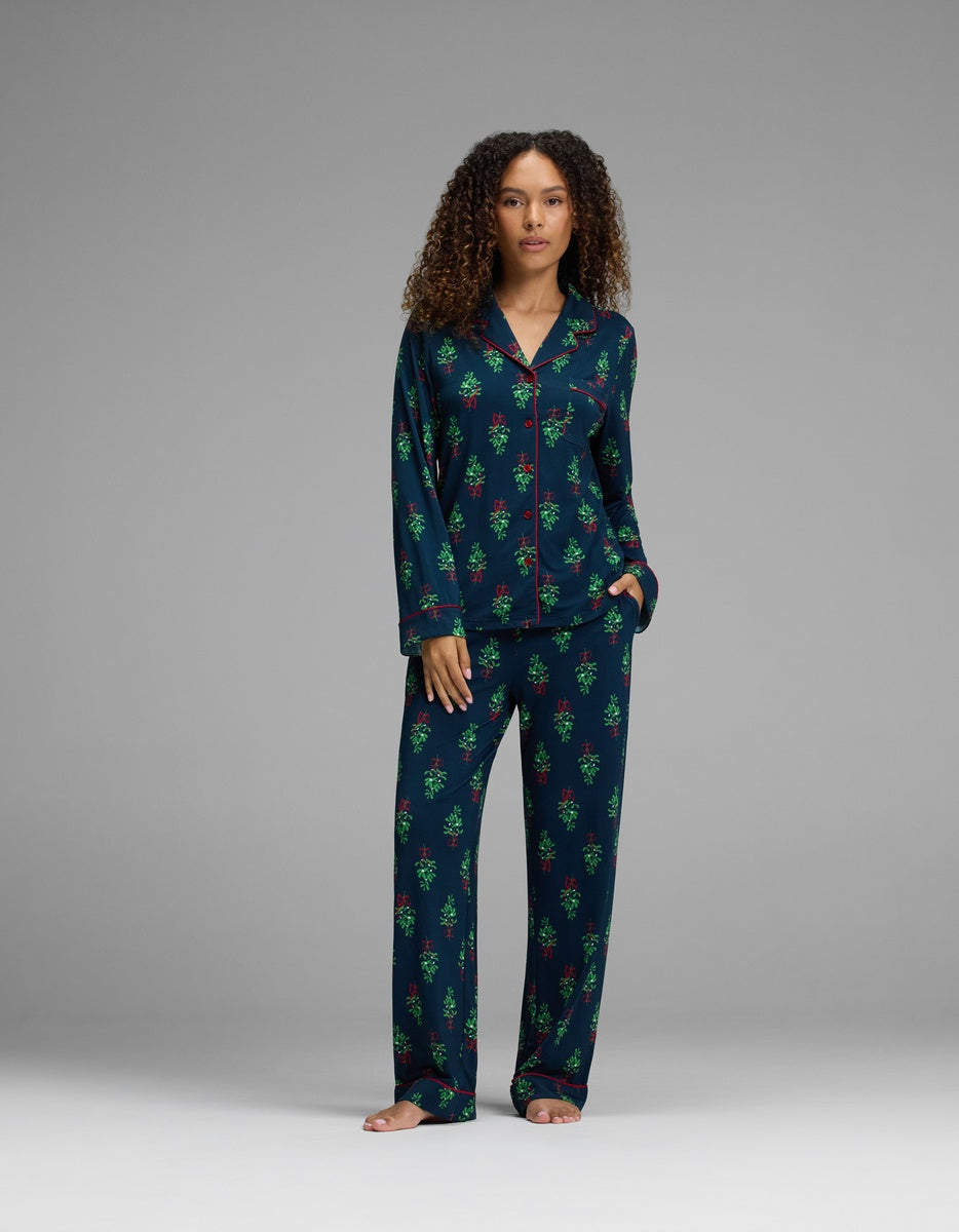 A woman wears a navy blue Cozy Earth Women’s Bamboo Stretch-Knit Long Sleeve Pajama Set with a red and green holiday-themed pattern.|Color:Obsidian Mistletoe