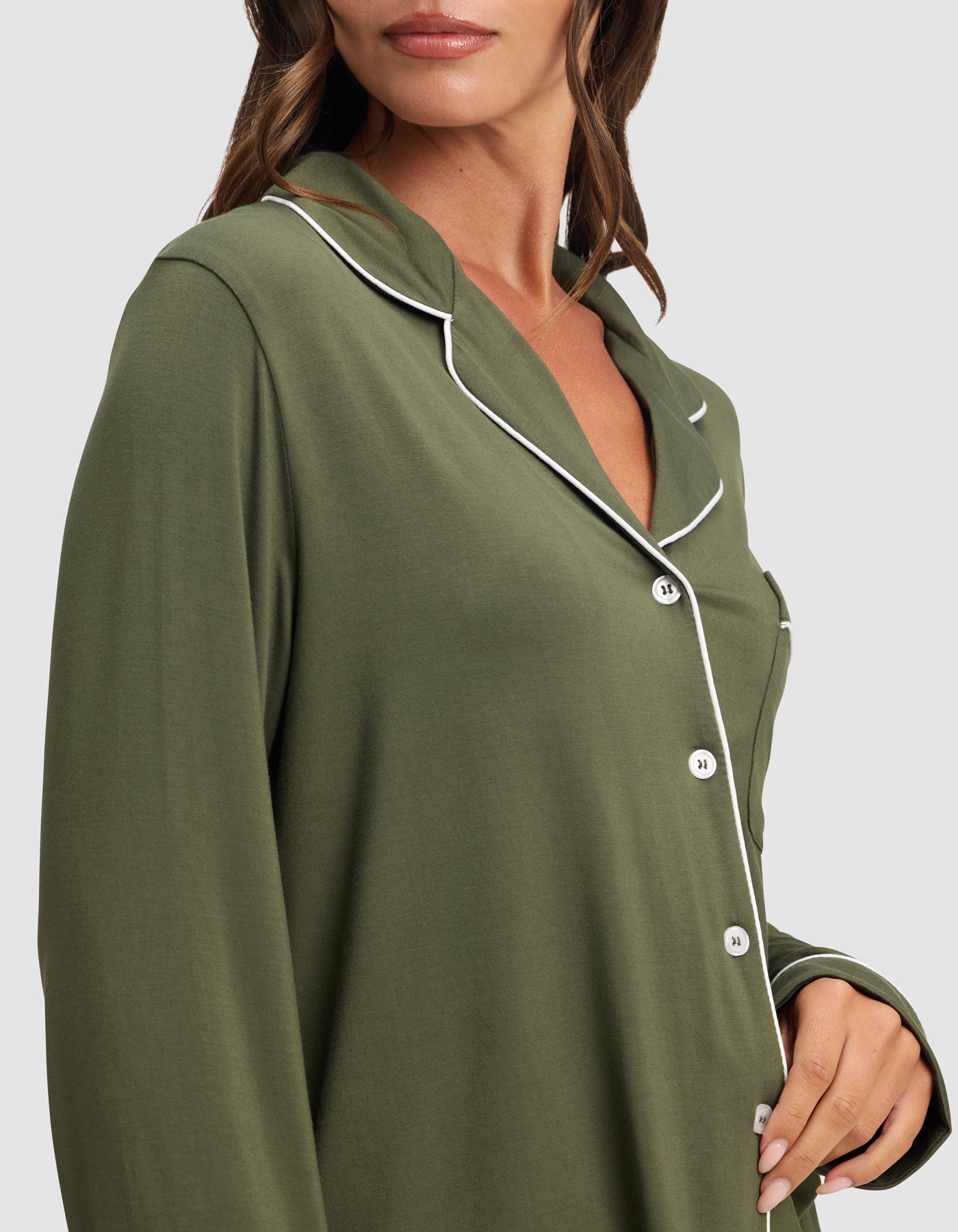 A woman wears the HIDE Women's Bamboo Stretch-Knit Long Sleeve Pajama Top in olive green with white piping and buttons, pictured from shoulders to hips with the collar and part of her face visible.
