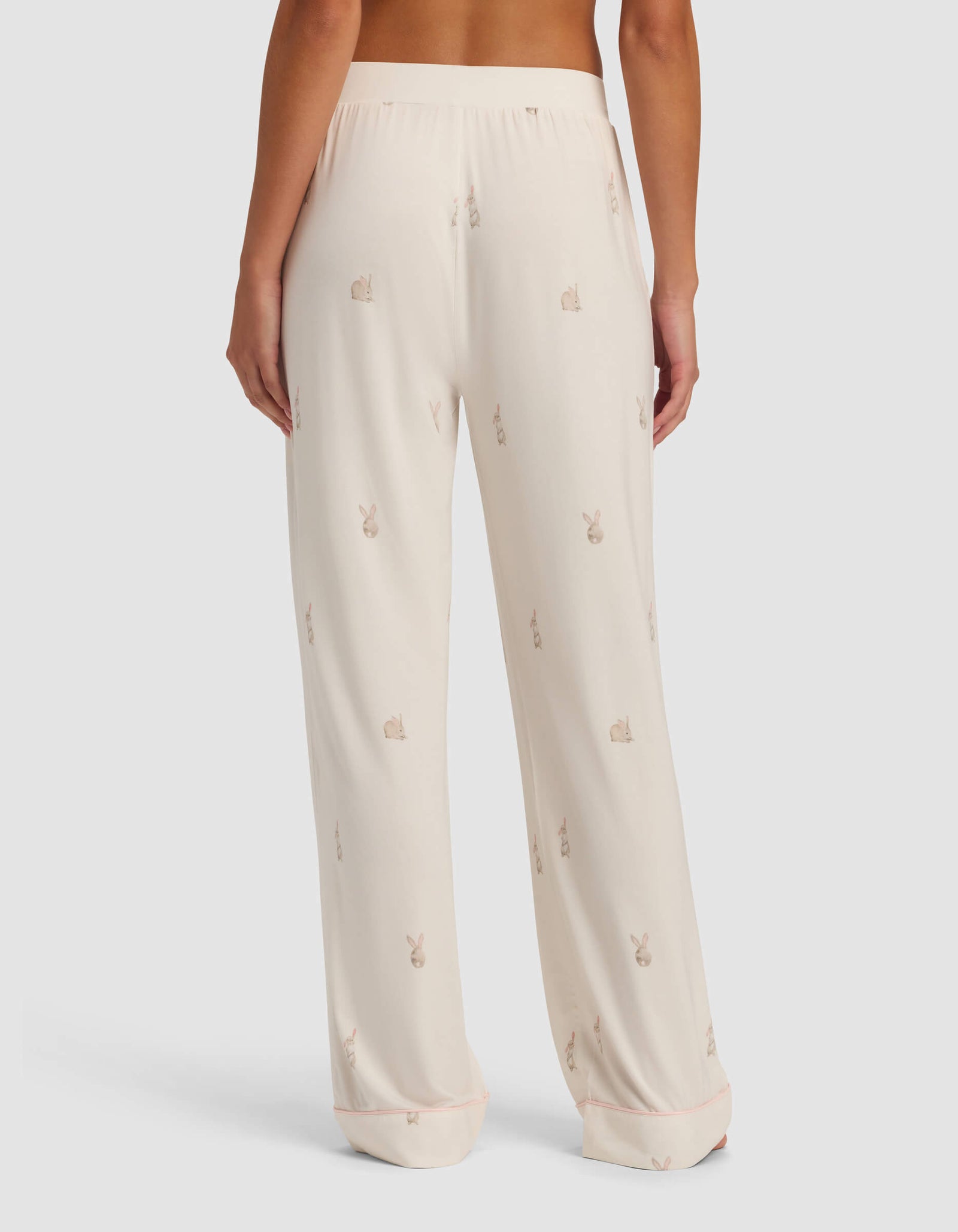 A person is shown from the back wearing Cozy Earth Women's Bamboo Stretch-Knit Pajama Pant in light cream with a small bunny print, against a plain white background.