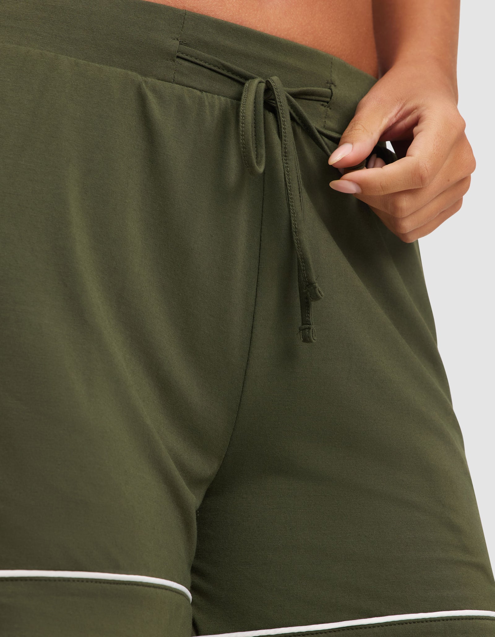 Close-up of a person adjusting the drawstring waist of HIDE's Women's Bamboo Stretch-Knit Pajama Short in olive green with white trim.