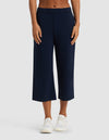 A person wearing Cozy Earth's Women's Brushed Bamboo Pull On Capri in navy blue with white sneakers and a bare midriff, standing against a plain light gray background.|Color:Navy