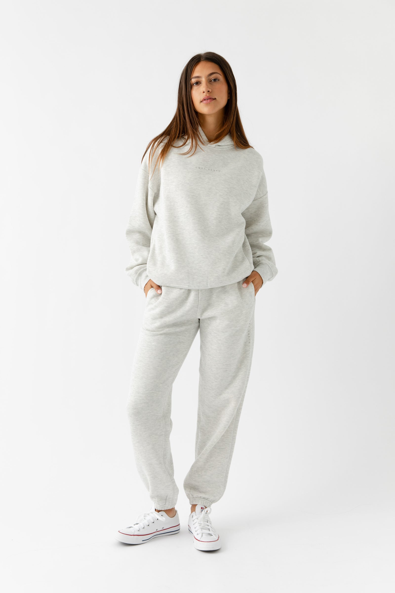 A woman poses confidently against a white background in Cozy Earth's Women's CityScape Hoodie & Sweatpant Set, her hands tucked into the pockets.|Color:Heather Grey
