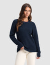 A woman with long brown hair models the Cozy Earth Women's Classic Crewneck in navy blue, paired with off-white pants. She stands against a plain light gray background, one hand in her pocket.|Color:Eclipse