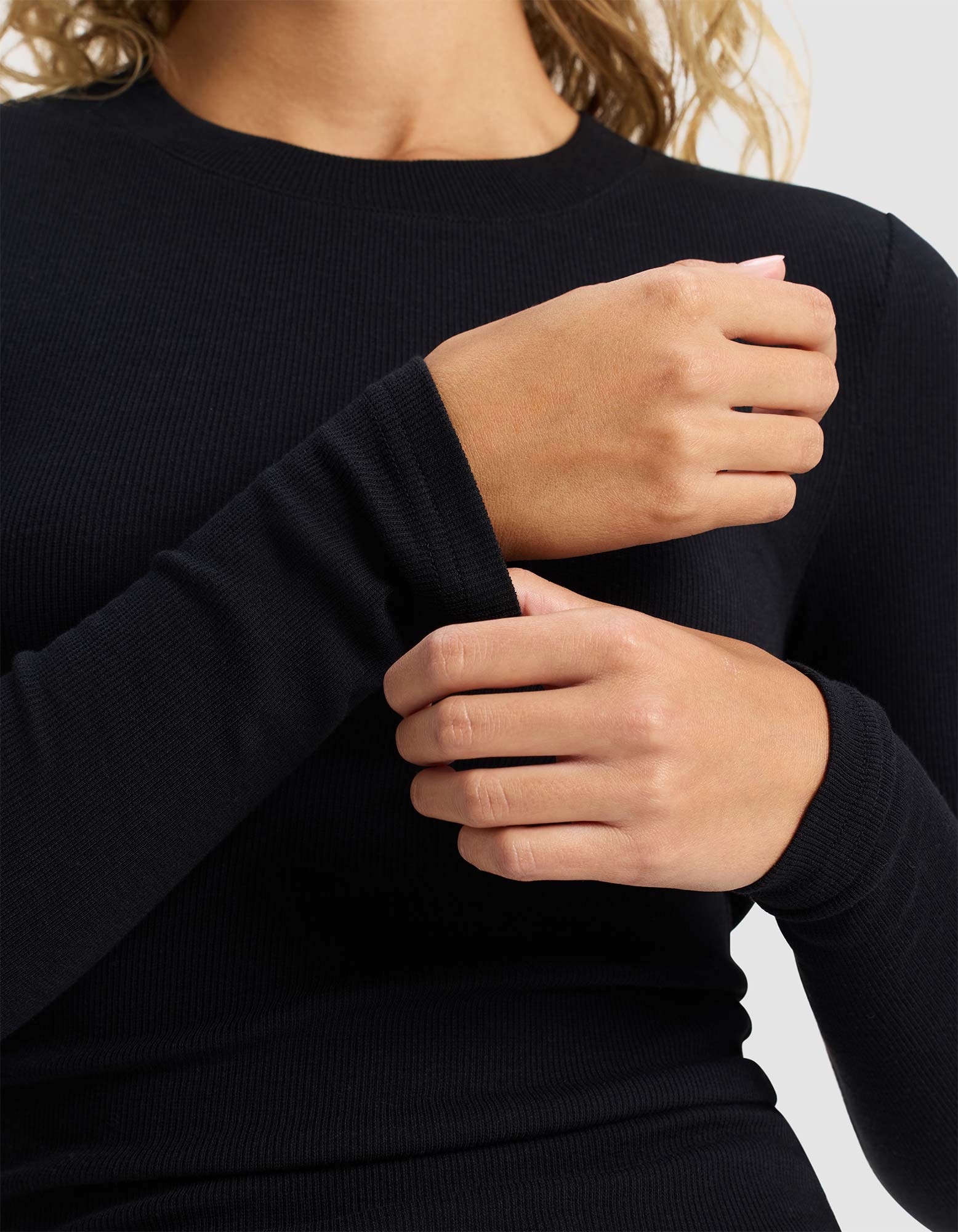 A person wearing Cozy Earth's Women's Fine Ribbed Long Sleeve Tee in black adjusts their sleeve; only the torso and hands are visible.