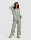 A woman models the Cozy Earth Women's Soft Woven Long Sleeve Pajama Set, featuring green and white stripes, paired with tan slippers, standing against a plain light background.|Color:Striped Jasper