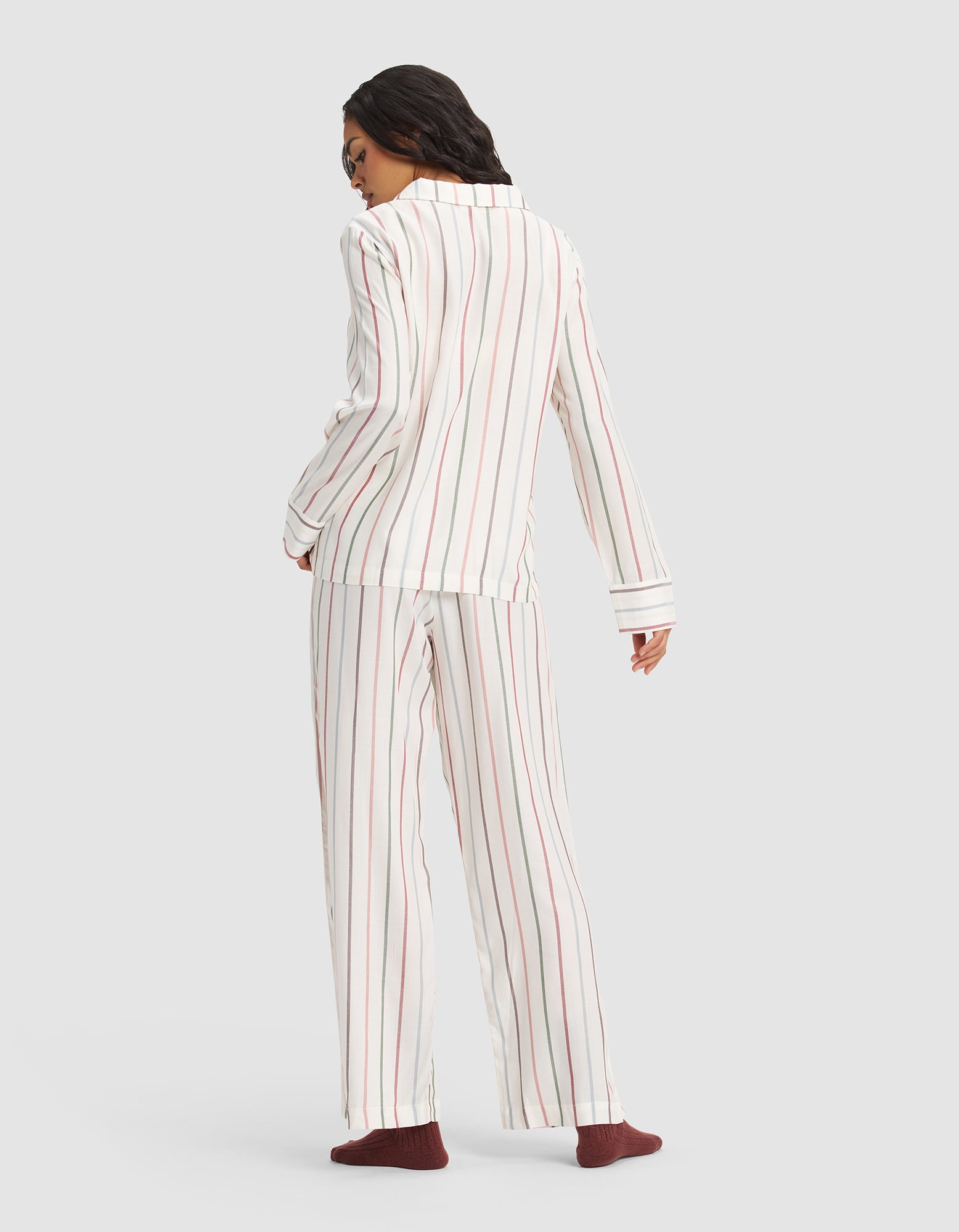 A person faces away, wearing the Cozy Earth Women's Soft Woven Long Sleeve Pajama Set in white with red and gray vertical stripes and dark red socks, set against a plain light gray background.|Color:Cottage Stripe