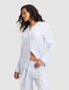 A woman stands sideways in a Cozy Earth Women's Soft Woven Long Sleeve Pajama Top, light blue and white striped, with buttons and matching pants, one hand in her pocket against a plain light background. |Color:Spring Blue Stripe