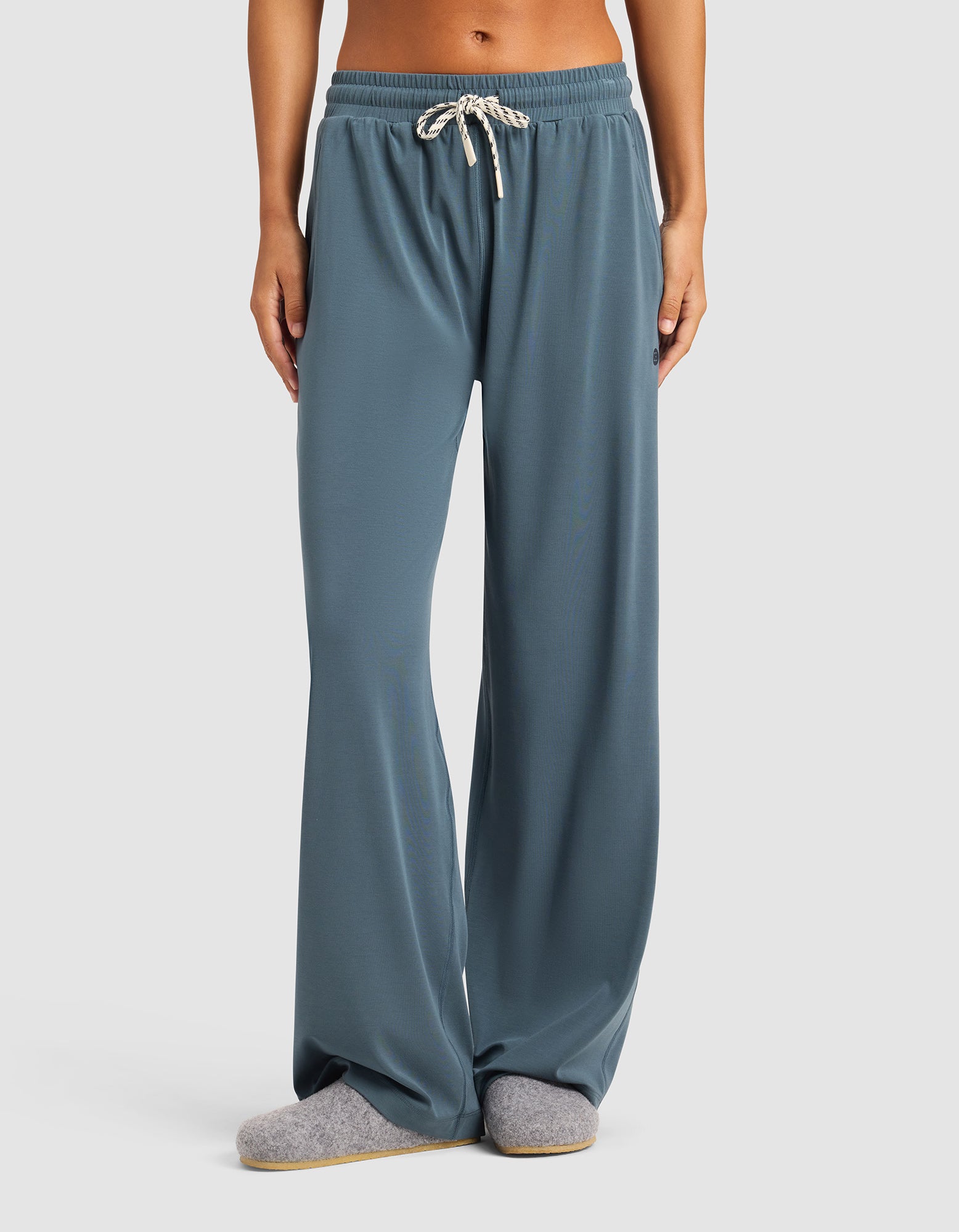 A person wears Cozy Earth's Women's Studio Wide Leg Pant in blue-gray, paired with gray slippers, standing against a plain light background. Only the lower half of the body is shown.|Color:Dawn