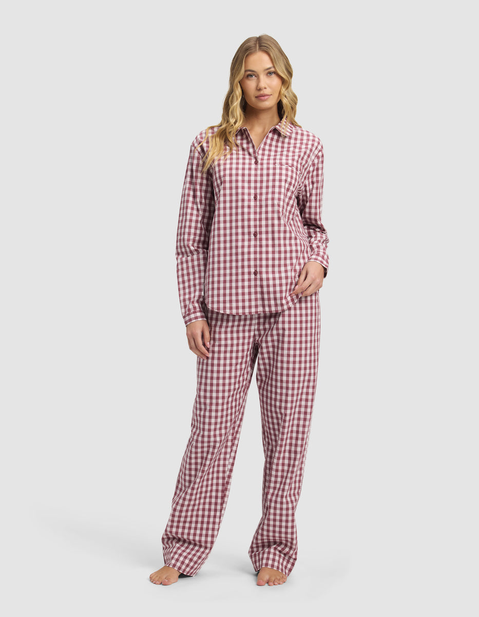 A woman stands barefoot in a Cozy Earth Women's Sutton Long Sleeve Pajama Set, featuring a red and white checkered button-up shirt and loose pants, against a plain light background.|Color:Mulberry Gingham
