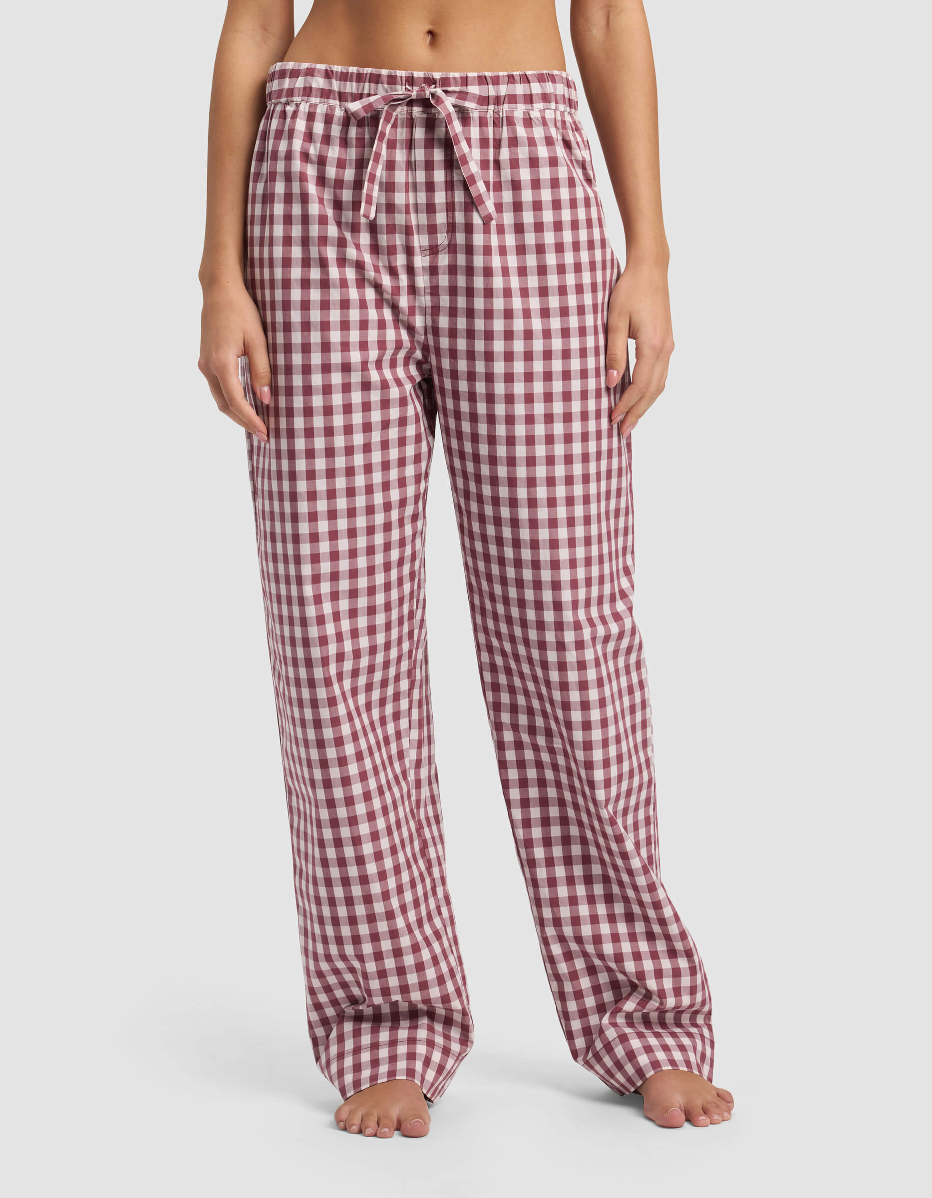 A woman stands barefoot wearing Cozy Earth Women's Sutton Pajama Pant, featuring a loose fit and red and white checkered pattern with a drawstring waistband, shown from shoulders down against a plain white background.|Color:Mulberry Gingham