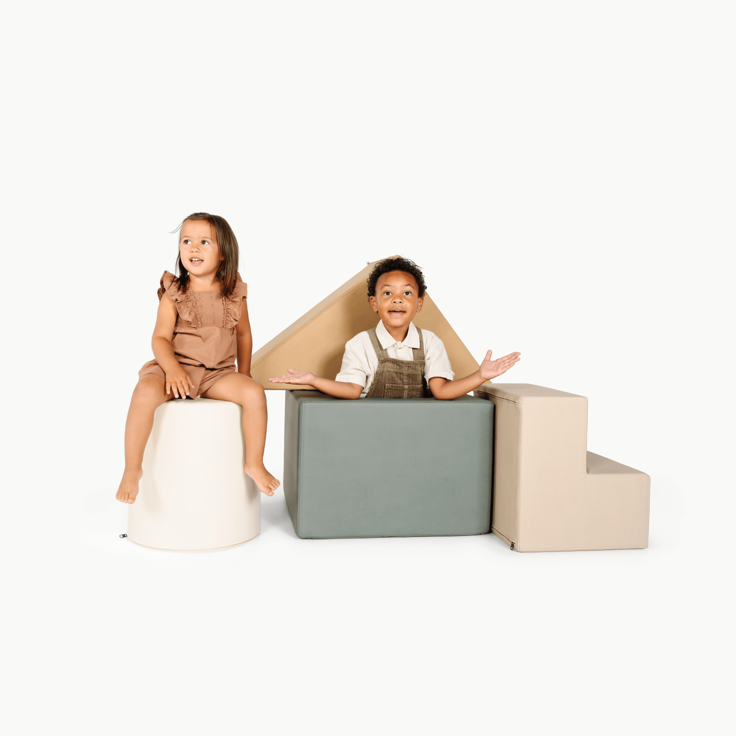 Two young children play on the Gathre Wholesale Block Playset, featuring soft, neutral-colored foam blocks in cylinder, cube, triangle, and stairs shapes, set against a plain white background.