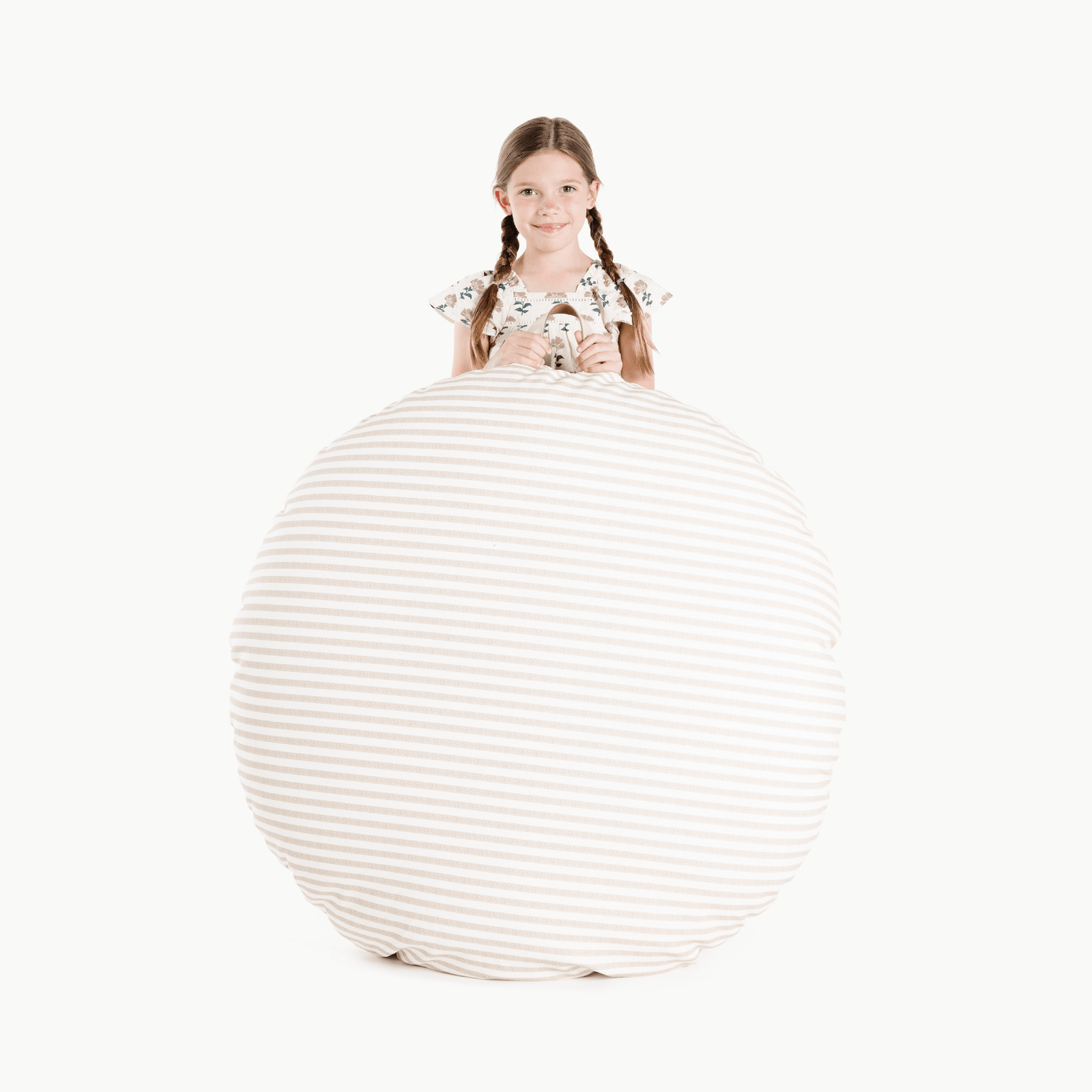A young girl with braided hair stands behind the Gathre Wholesale Floor Cushion in Cafe Stripe, mostly hidden except for her head and hands, against a plain white background.