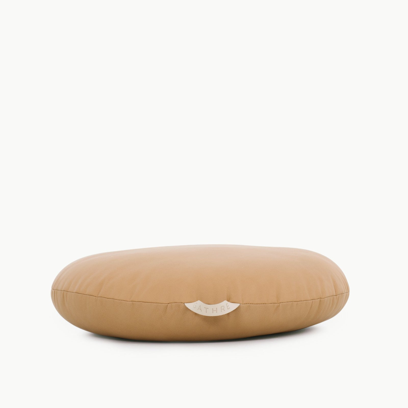 The Gathre Wholesale Floor Cushion is a tan, round, flat cushion featuring a smooth surface and a small fabric label at the front, displayed on a plain white background.