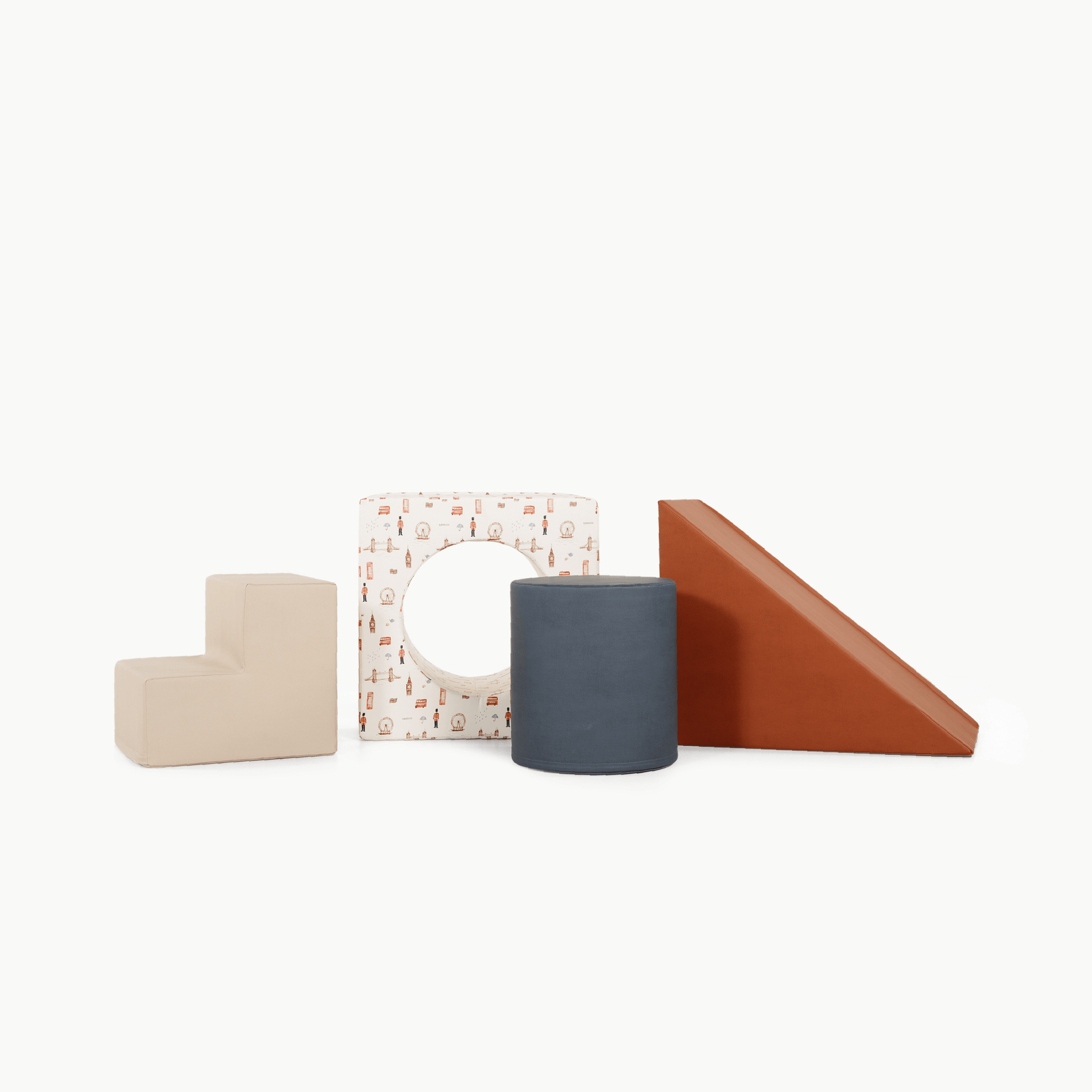 The Gathre Wholesale Block Playset features four foam shapes in London, Nightfall, Rust, and Millet—an L-shaped block, a patterned square with a circular cutout, a dark blue cylinder, and a wedge—all arranged in a row on white.