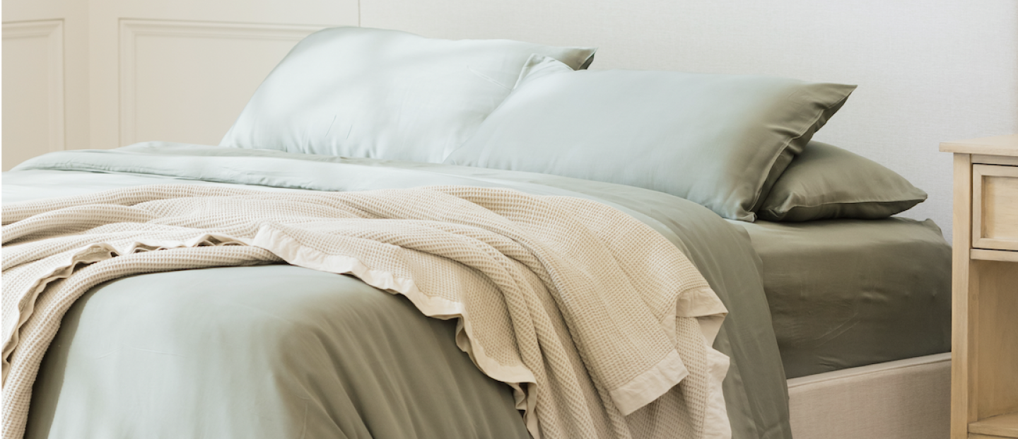 Photo of bed made with sage bedding with waffle blanket draped over it