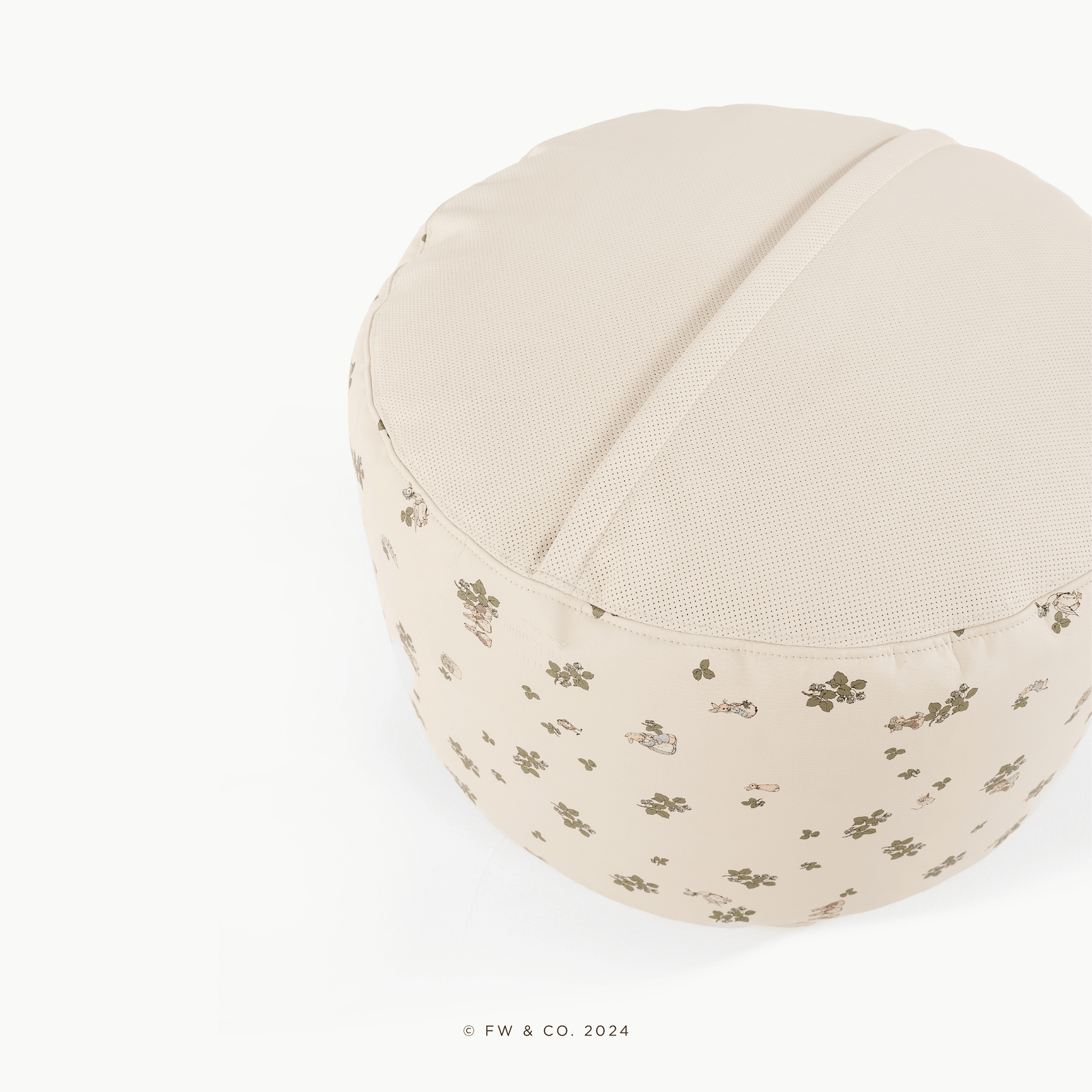 The Gathre Wholesale Pouf is a round, beige cushion featuring a textured top and sides with a subtle floral and character print, shown on a plain white background.