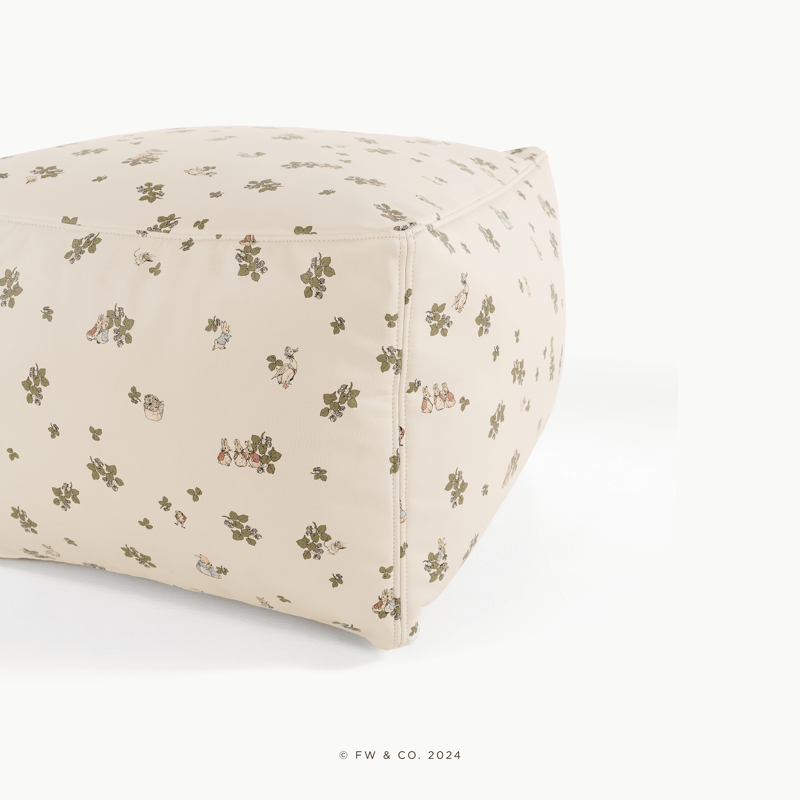 The Gathre Wholesale Pouf is a beige, cube-shaped cushion featuring small green floral and animal illustrations, displayed against a white background. Soft and decorative, it adds charm to any space.