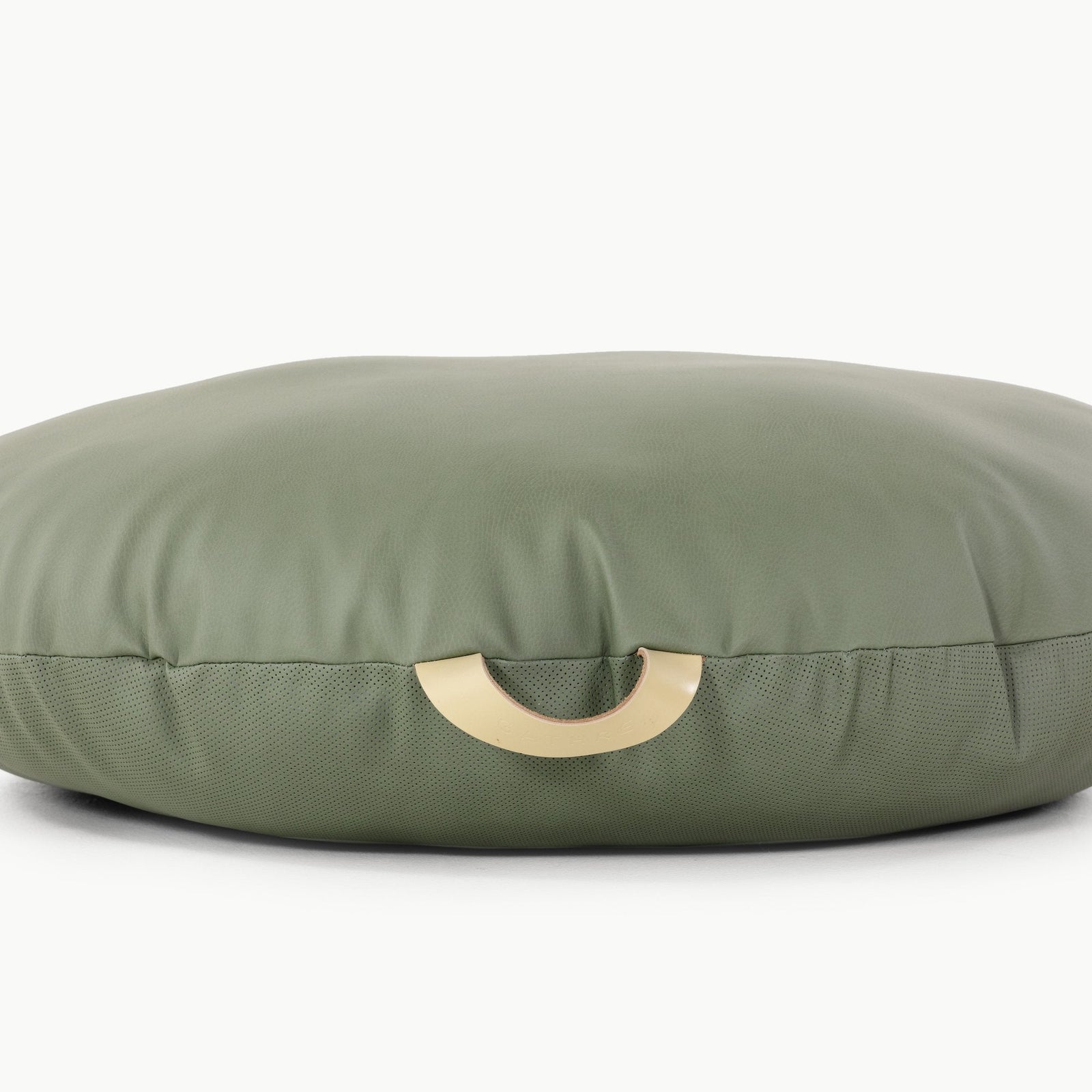 The Gathre Wholesale Floor Cushion is round and green with a smooth texture and features a gold, crescent-shaped handle on its side, shown against a white background.