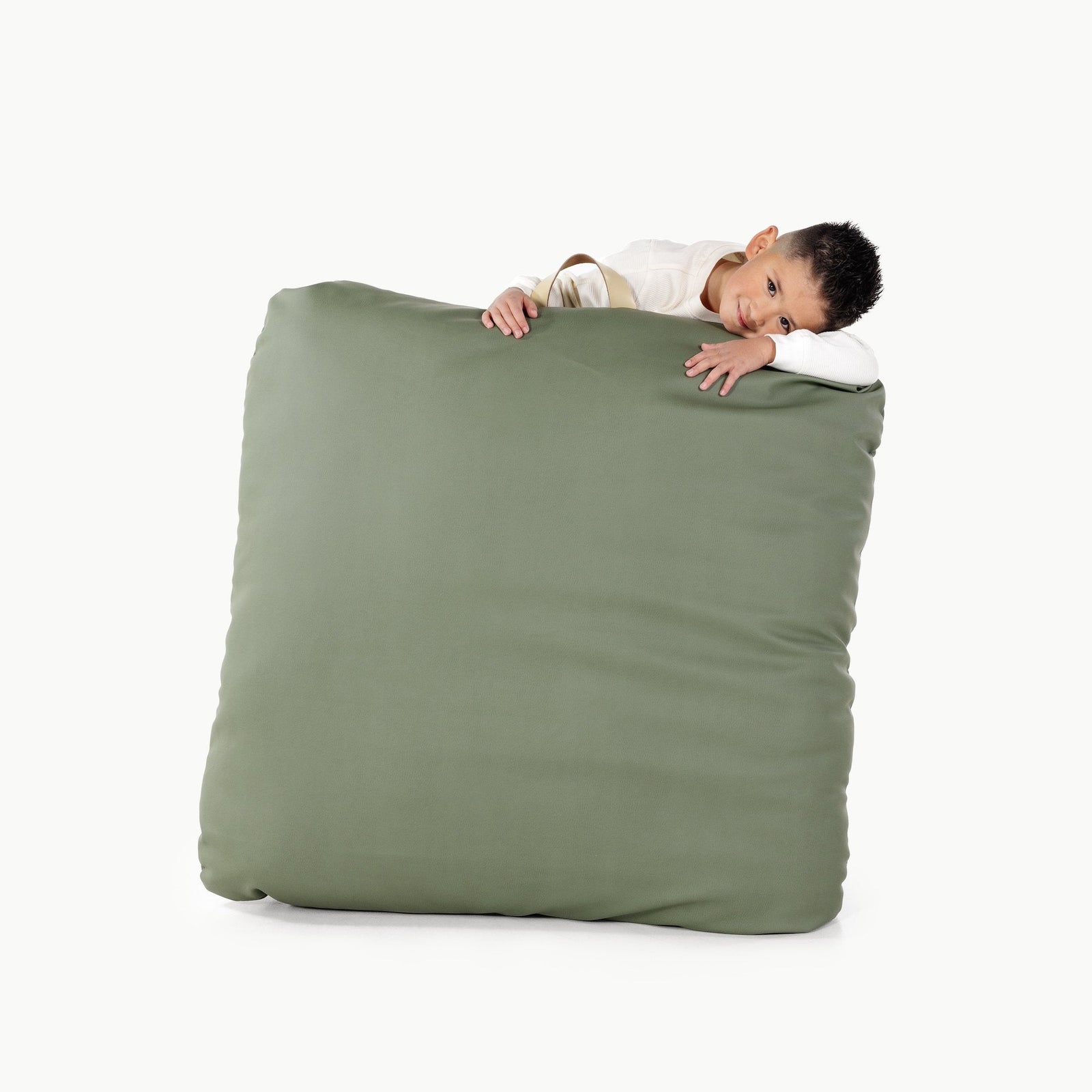 A young boy leans over and rests his head on the Gathre Wholesale Floor Cushion in Thyme, looking relaxed against a plain white background.