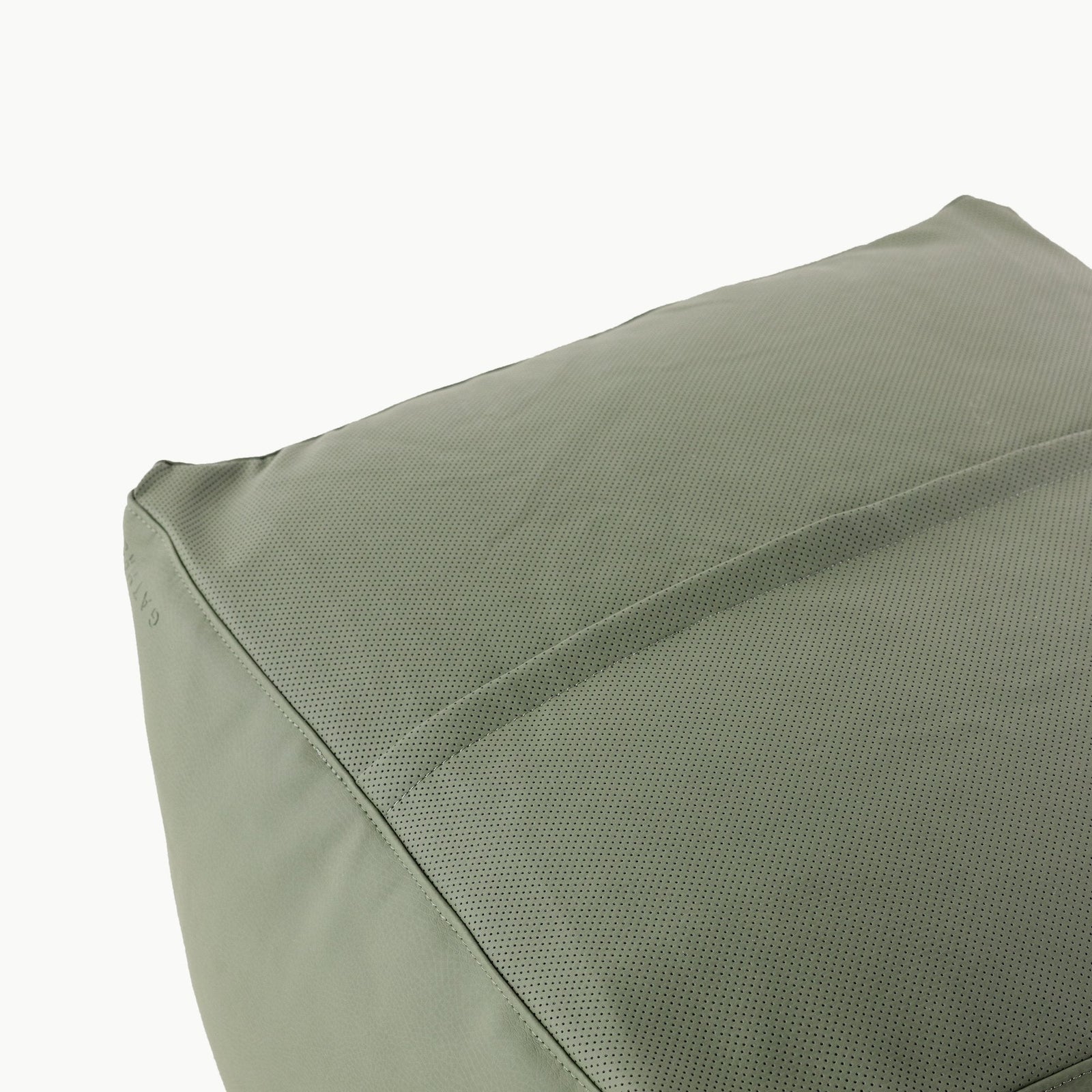 A close-up of the Gathre Wholesale Pouf shows its green, fabric-covered surface with textured perforations and a smooth seam running across it.