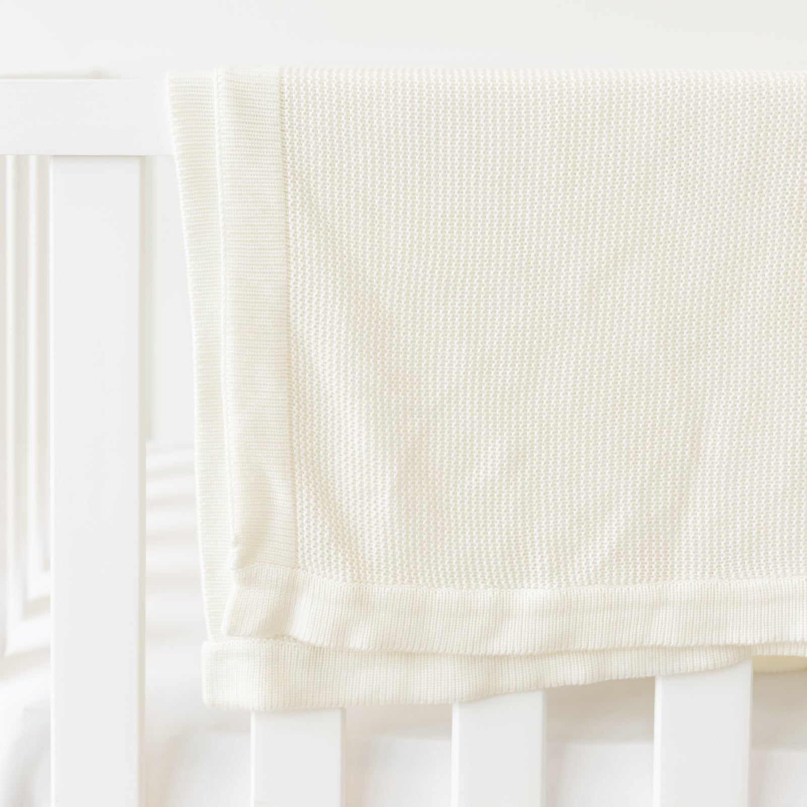 Ivory Cloud Knit Baby Blanket draped over crib 