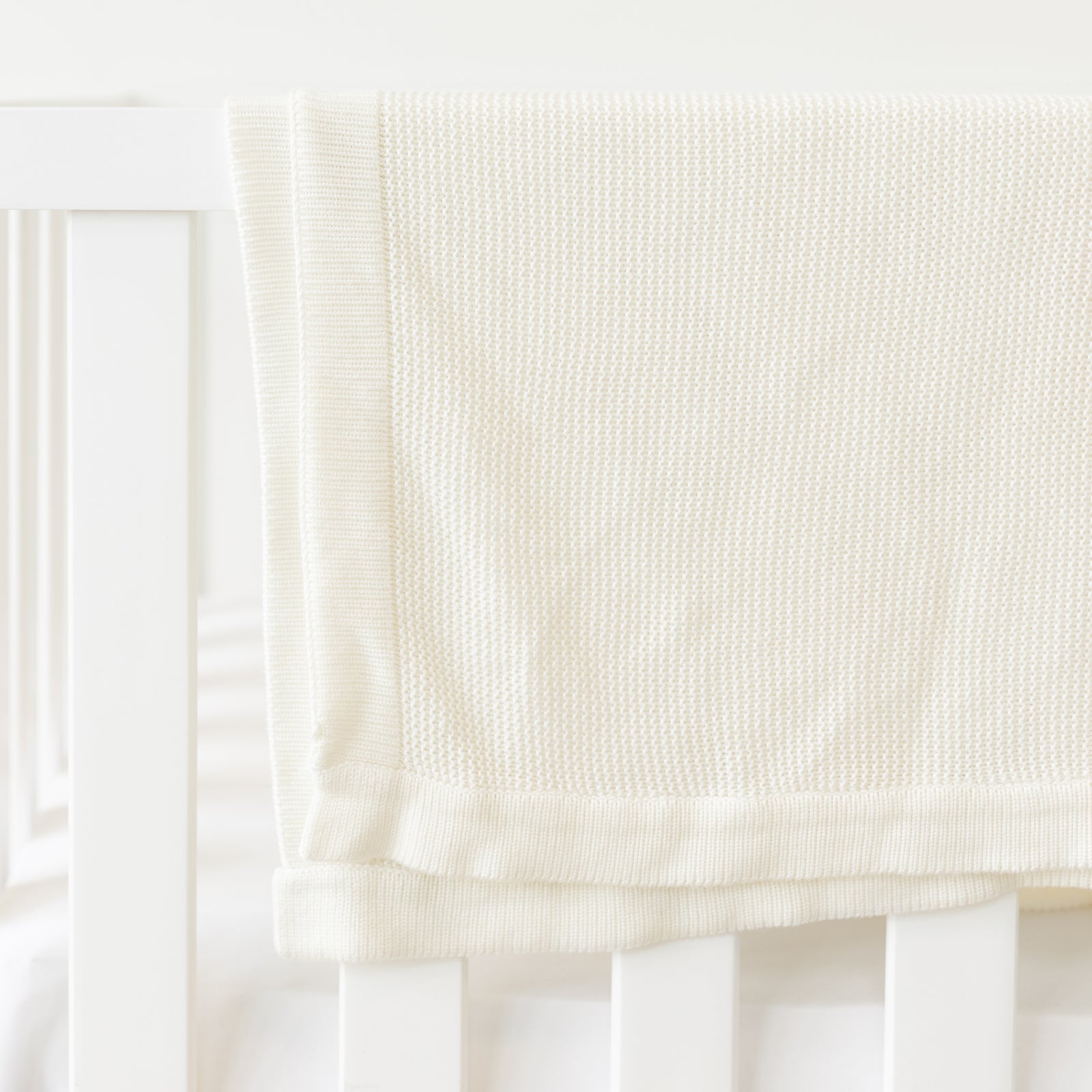 Ivory Cloud Knit Baby Blanket draped over crib