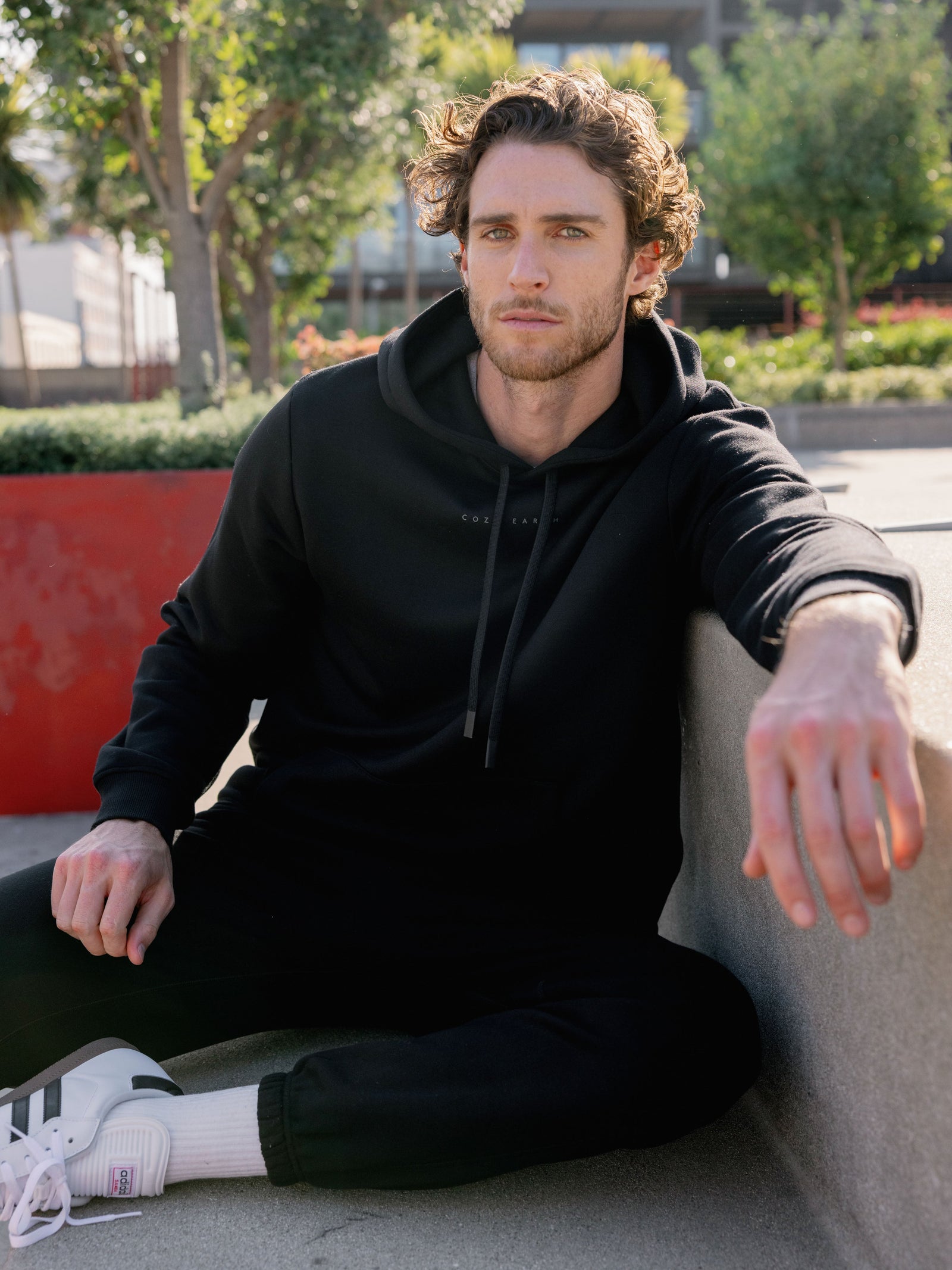 Man sitting on city bench wearing black cityscape hoodie and sweats