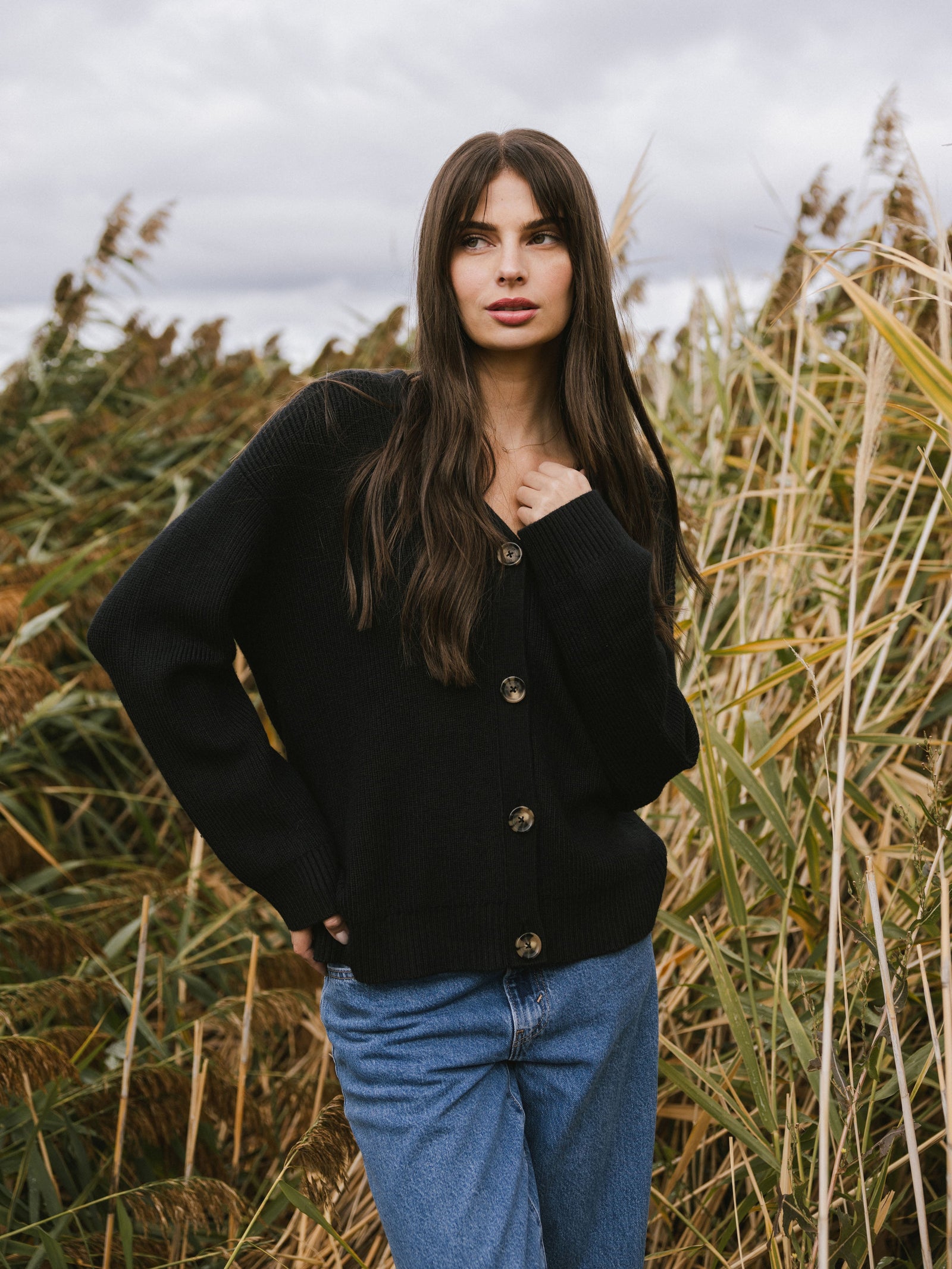 A woman stands surrounded by tall grass wearing Cozy Earth Classic Cardigan in Black