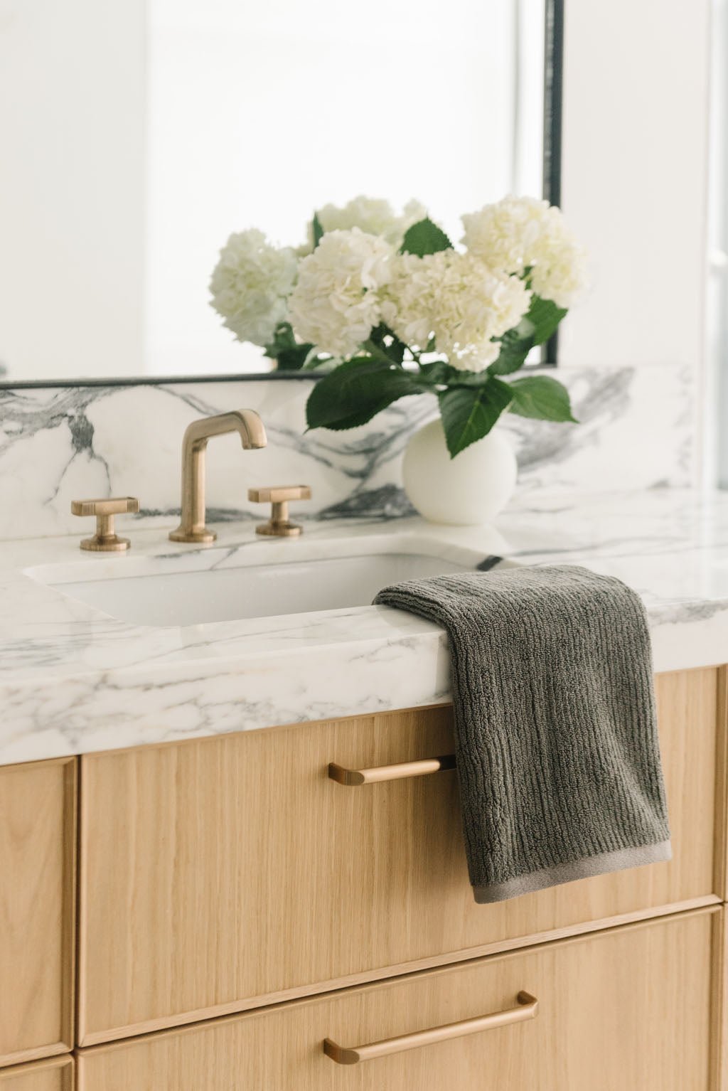 Ribbed Terry Hand Towels in the color charcoal. Photo of product taken with the product draped over a white marble sink. 