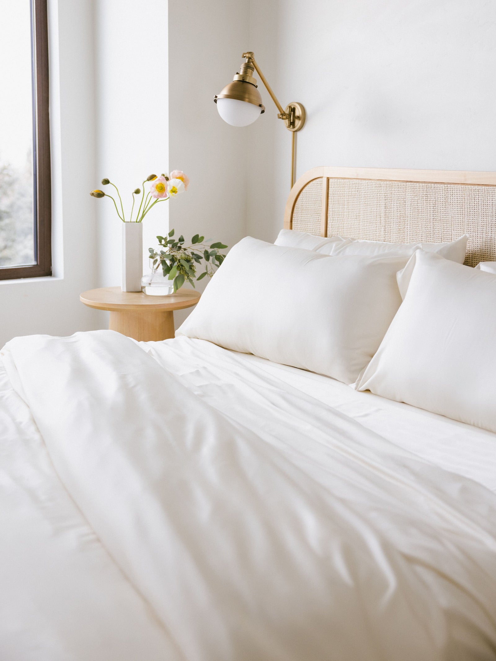 Bed with creme bedding with a lamp and plants to the side