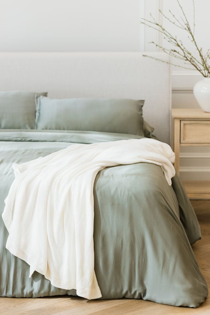 Ivory cloud knit blanket draped over bed with sage bedding
